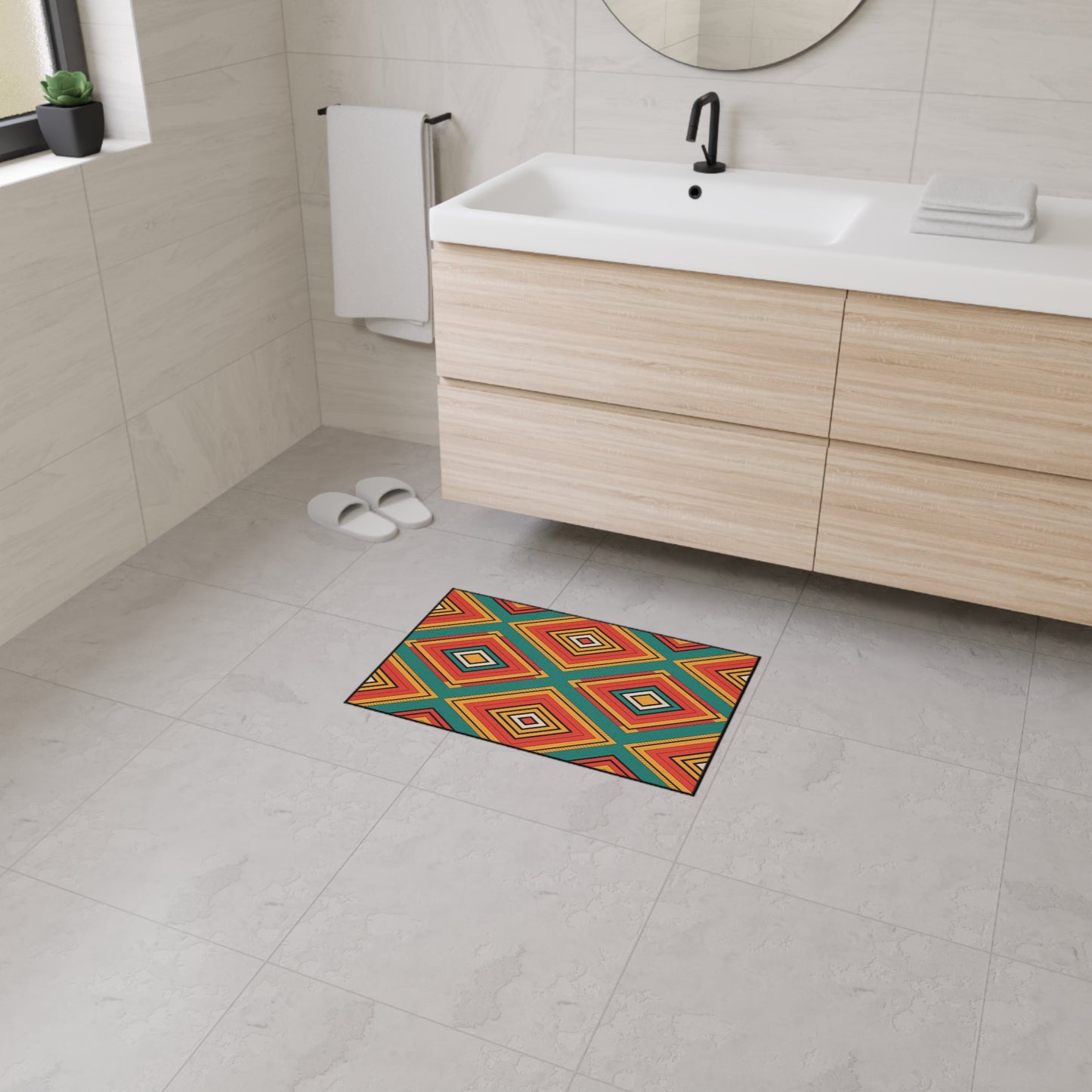 A modern bathroom with light-colored tile floors, light wood vanity, white sink, black faucet, white towels, slippers, and a vibrant African-inspired non-slip mat featuring a geometric diamond pattern in red, yellow, orange, blue, and green.