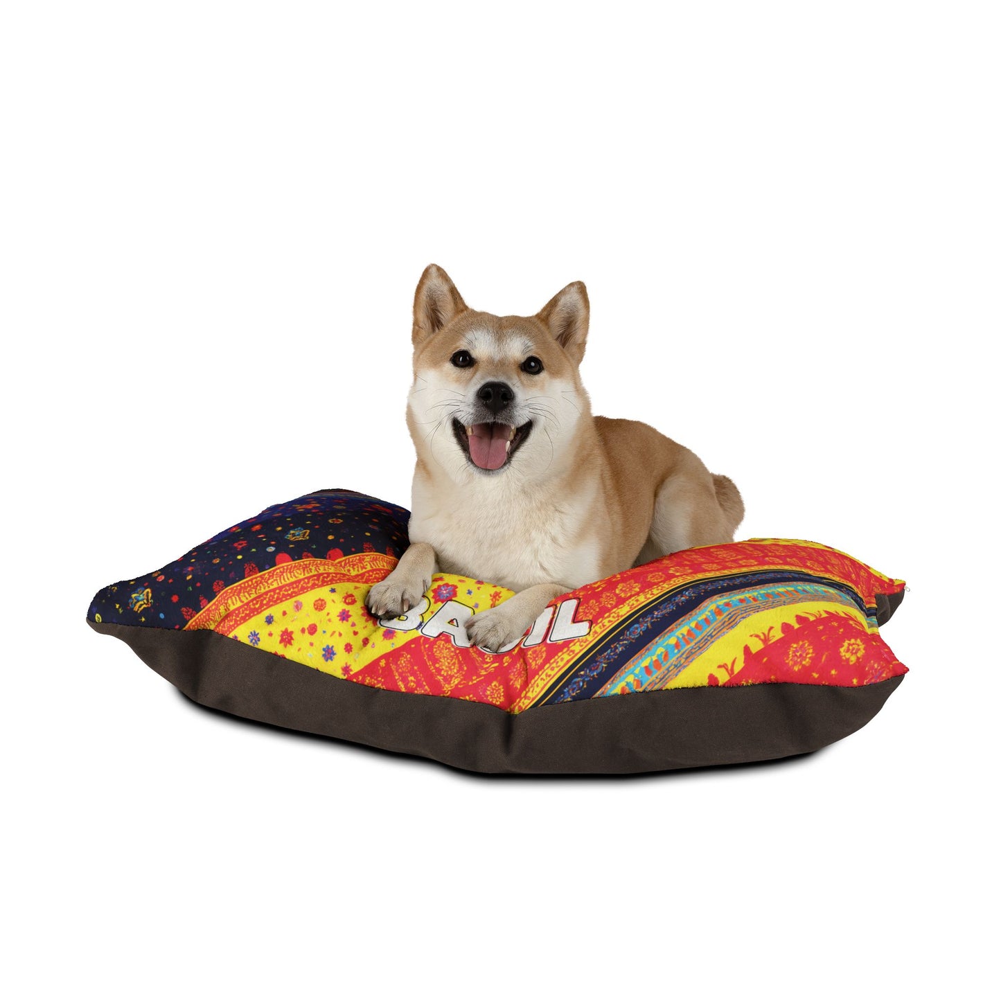 A happy Shiba Inu dog lies on a colorful, African-inspired patterned cushion with red, yellow, and blue designs. The thick, comfy cushion has a dark brown base. The dog faces forward, mouth open and tongue out, looking cheerful. White background.