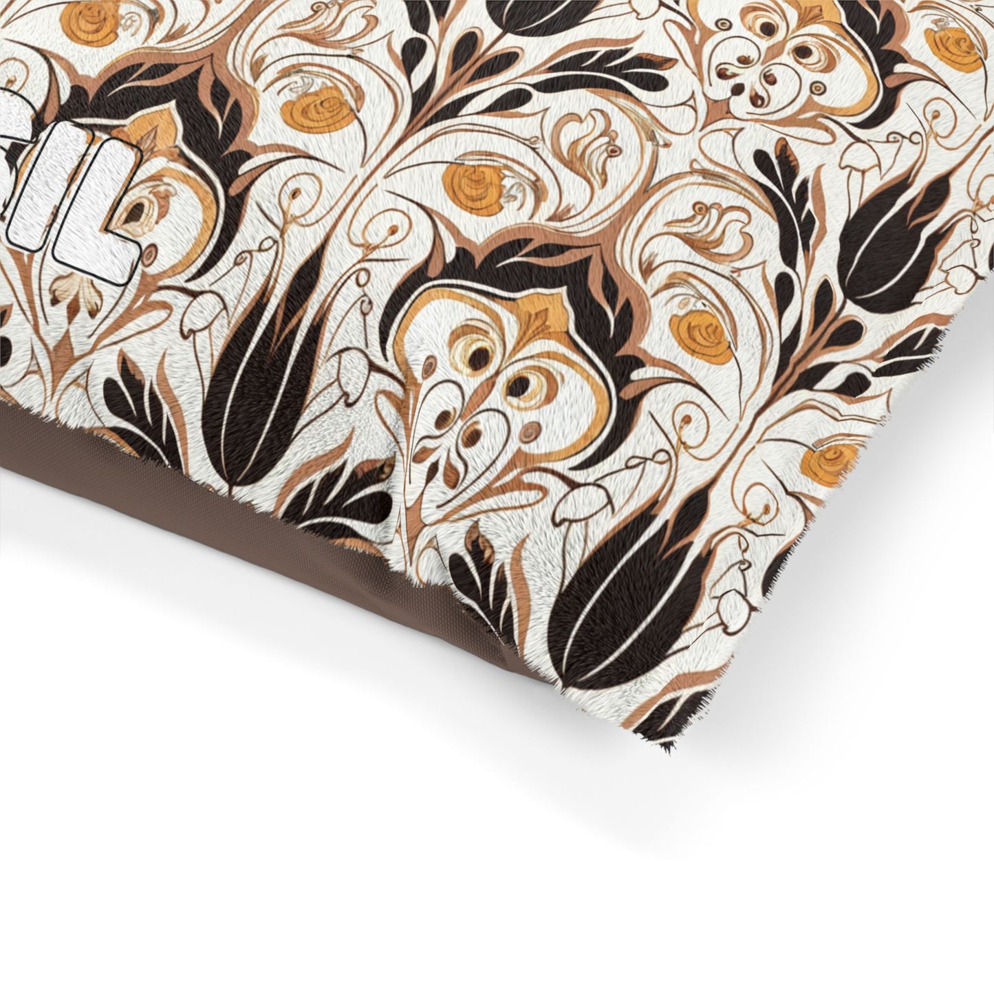 A close-up of an African-inspired fabric with an ornate, floral pattern in shades of black, gold, and beige. Curving vines and stylized flowers fill the design. Part of white block lettering is visible at the top left, with a frayed fabric corner.