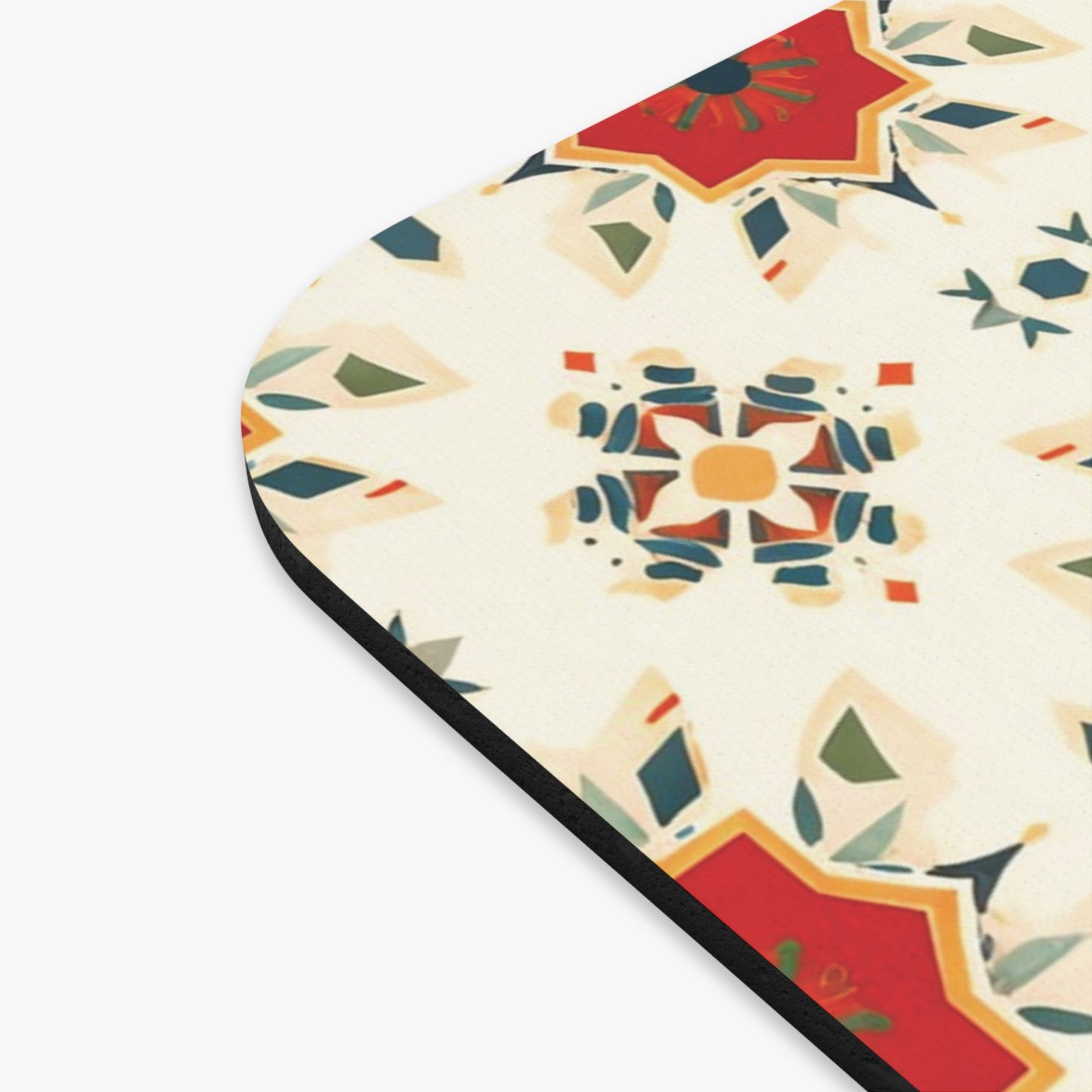 A close-up of an African-inspired mouse pad’s corner, featuring a geometric, kaleidoscope-style pattern in red, blue, green, and tan on a cream background. The design includes star and petal-like shapes with a rounded black edge visible on the left.