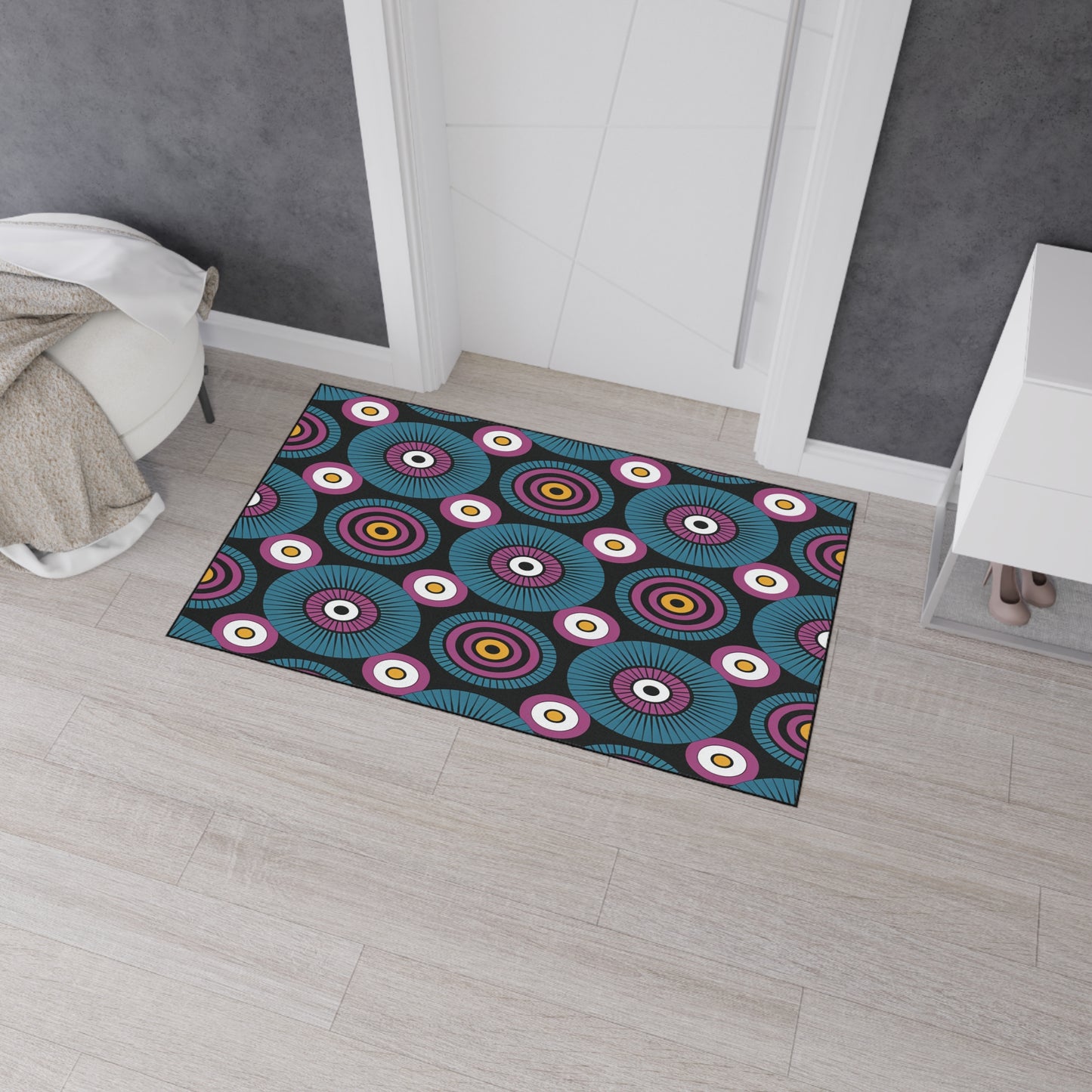 A rectangular doormat with a bold, colorful pattern of concentric circles in blue, purple, red, yellow, and white brings African-inspired aesthetics to a light wood floor. This custom floor mat features non-slip rubber backing for added safety.