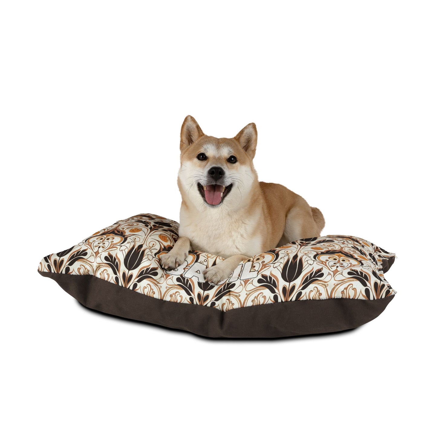 A tan Shiba Inu dog with a happy expression lies on a large, African-inspired cushion featuring a brown and beige floral pattern with a dark brown border, set against a plain white background.