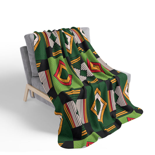 A gray armchair is draped with an African-inspired fleece blanket featuring geometric diamond and rectangular patterns in red, yellow, white, and black on a green background—perfect for adding bold, cozy home decor to a space. The background is plain white.