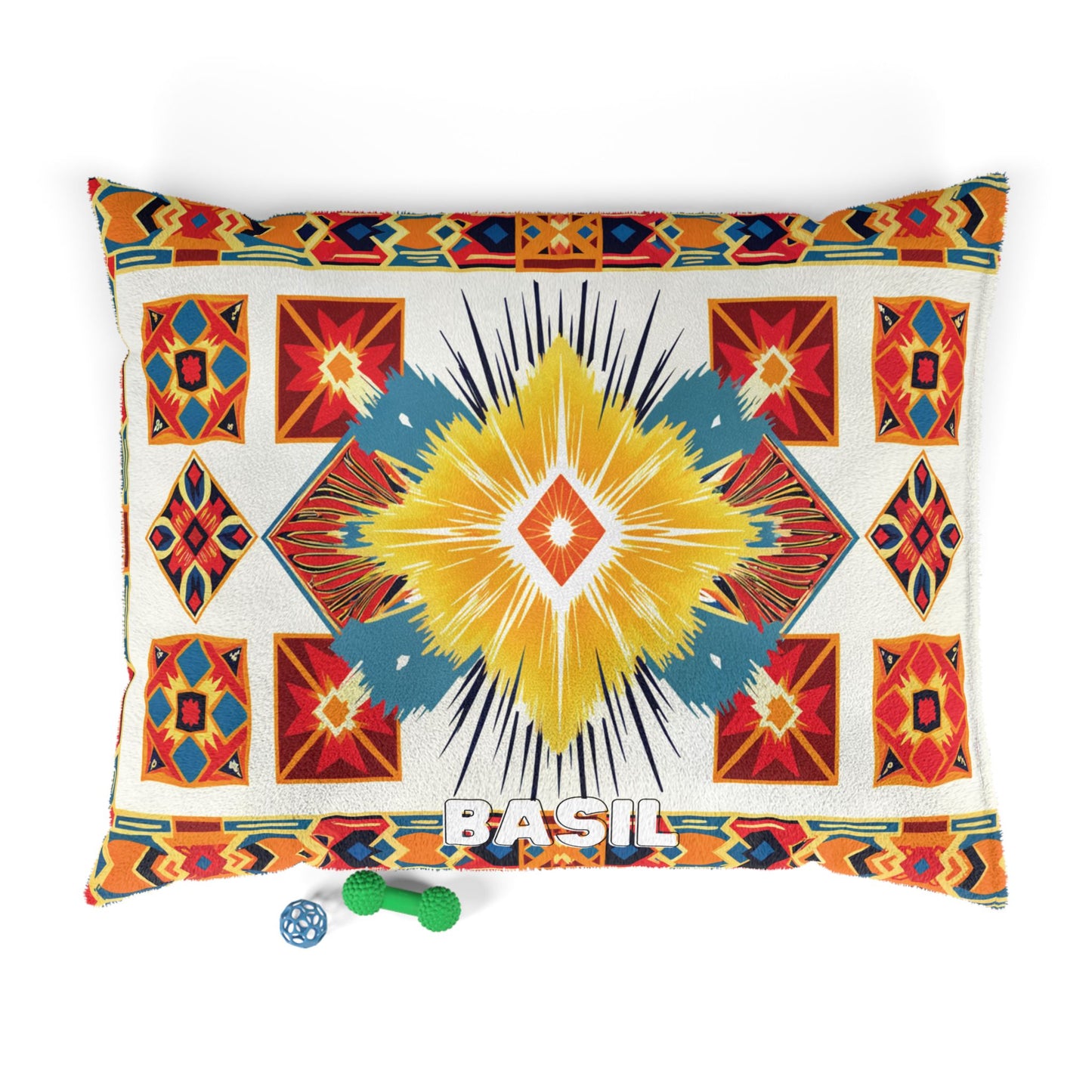 A rectangular pillow with a vibrant, African-inspired geometric pattern in red, yellow, turquoise, and orange. BASIL is written in white at the bottom center. Two small dog toys—a green bone and a blue ball—sit beside the pillow on a white background.
