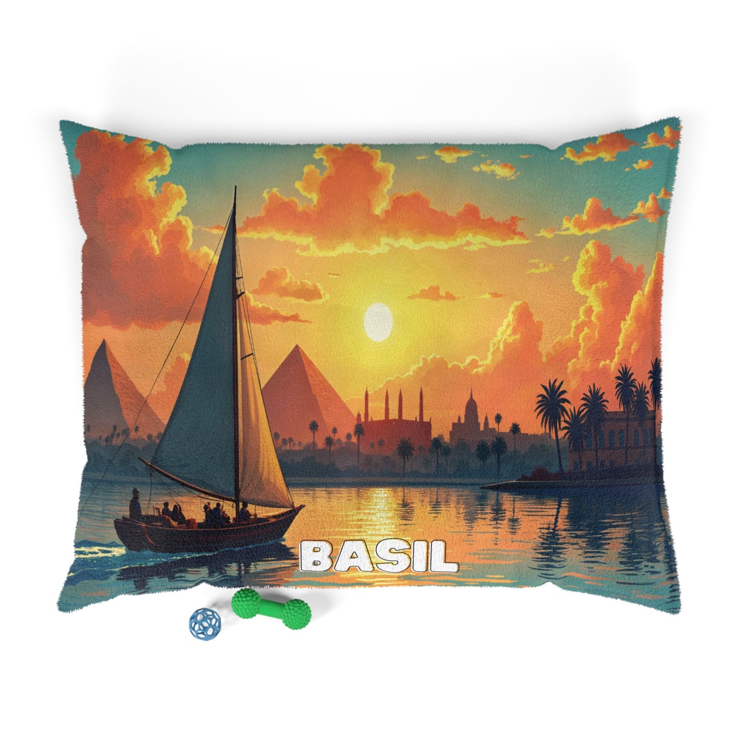 A decorative pillow with an illustration of a sailboat on a river at sunset, featuring pyramids and palm trees in the background. Two dog toys lie nearby, hinting at luxurious comfort—perfect alongside personalized pet beds and cozy spaces.