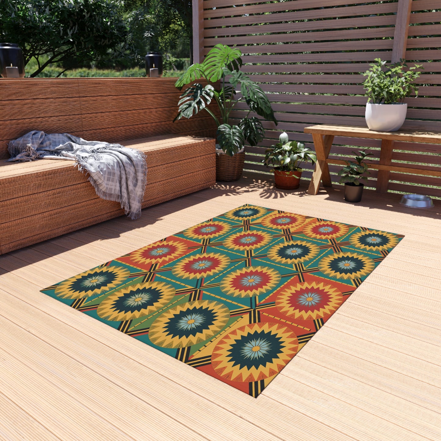 A cozy patio with light wooden flooring features an African-inspired outdoor rug with no-slip backing, a wicker bench with a gray throw, potted plants, and a wooden slat privacy screen. Sunlight and greenery complete this serene outdoor setting.