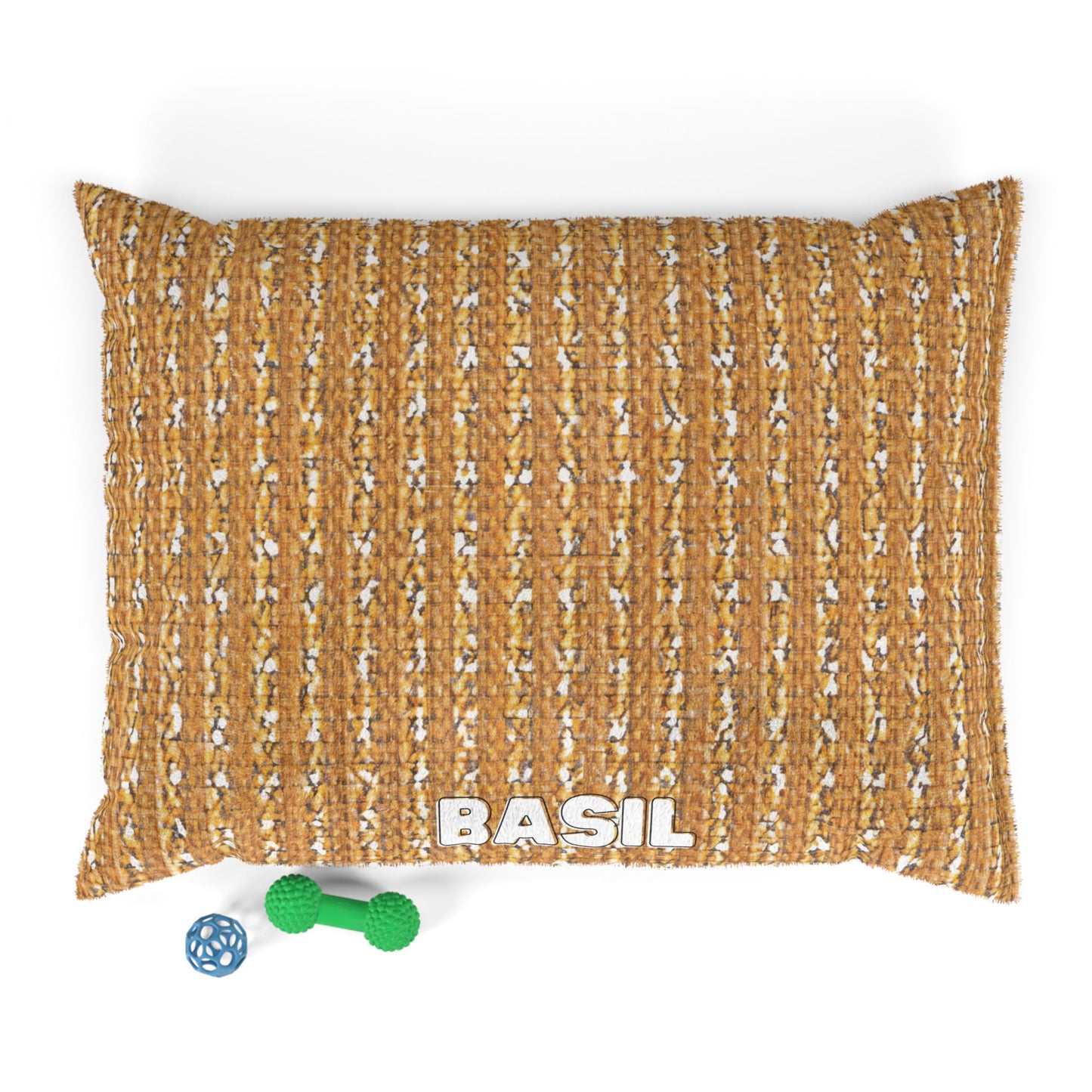 A rectangular, textured brown custom dog bed with BASIL in bold white letters at the front. Two dog toys—a blue ball and a green bone—are placed on a white surface beside this stylish pet bed, photographed from above.