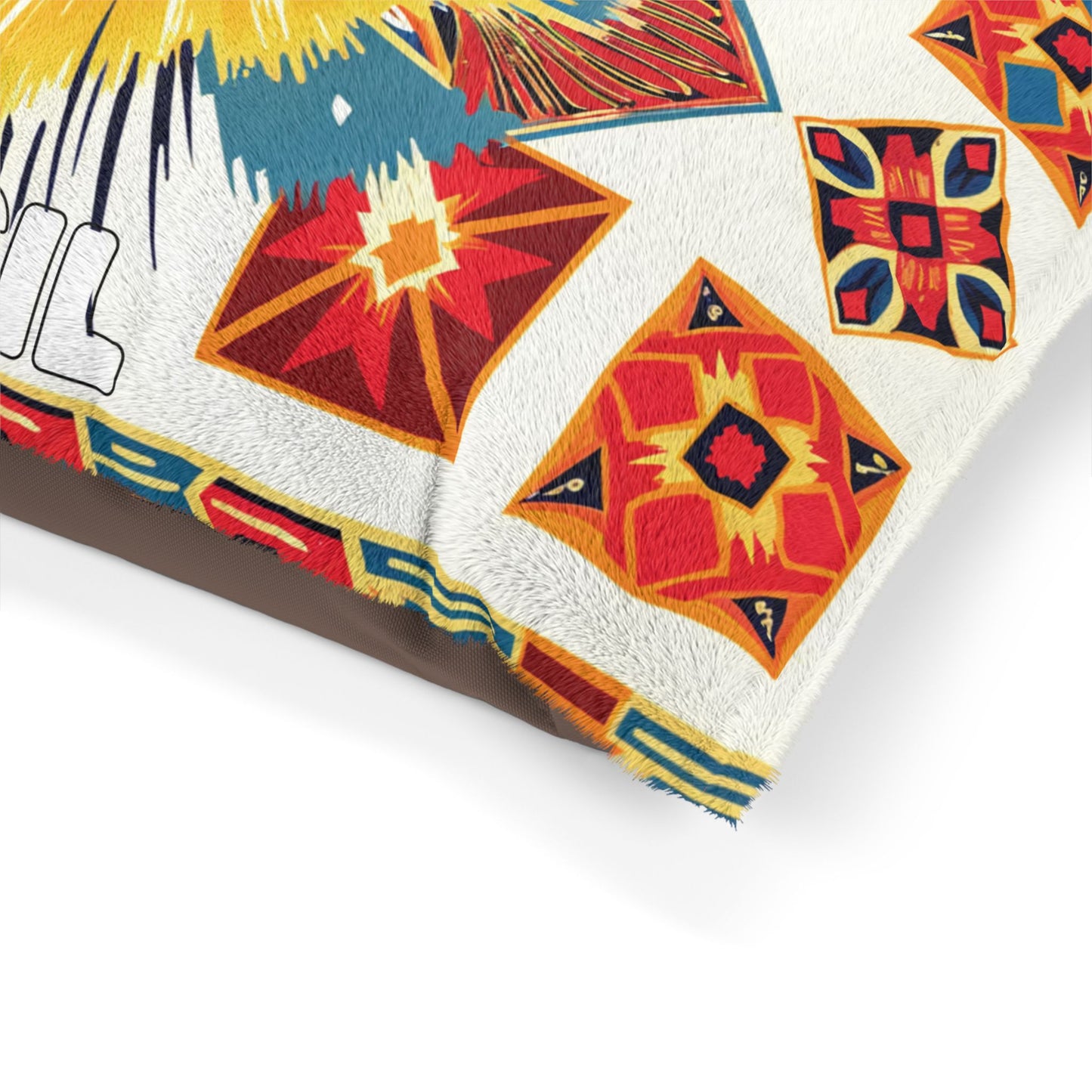 Close-up of a fabric pillow featuring an African-inspired pattern of colorful diamond and square shapes in red, orange, yellow, and blue. The pillow’s edge has a faux-fur texture and a partial view of bold, black outlined text on white.