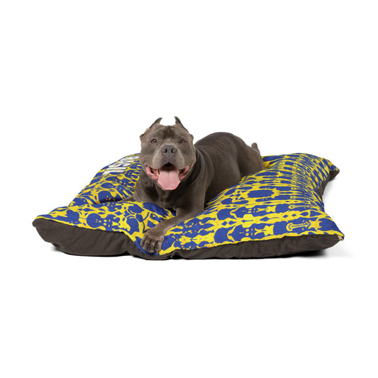 A gray dog with cropped ears lies happily on a large, colorful dog bed featuring durable construction. The bed boasts a vibrant blue and yellow pattern, dark brown underside, and the relaxed pup looks content against a white background.