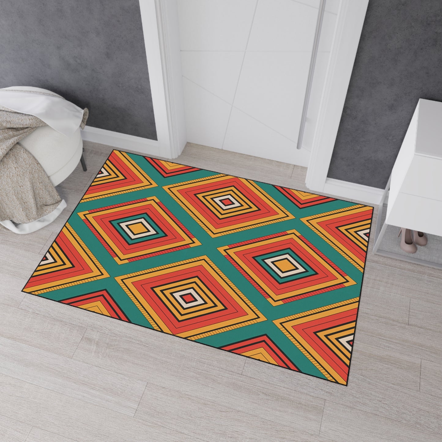 A colorful geometric rug with African-inspired aesthetics features red, yellow, orange, black, and teal diamond patterns. It lies on light wood flooring near a white door and chair draped with a beige blanket. A white cabinet with shoes is on the right.