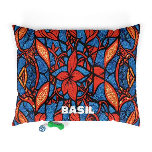 A rectangular custom pet pillow with a bold blue, red, and orange abstract leaf pattern. The name BASIL is printed in large white letters at the bottom center. Two small dog toys, a green bone and a blue ball, are placed below the pillow.