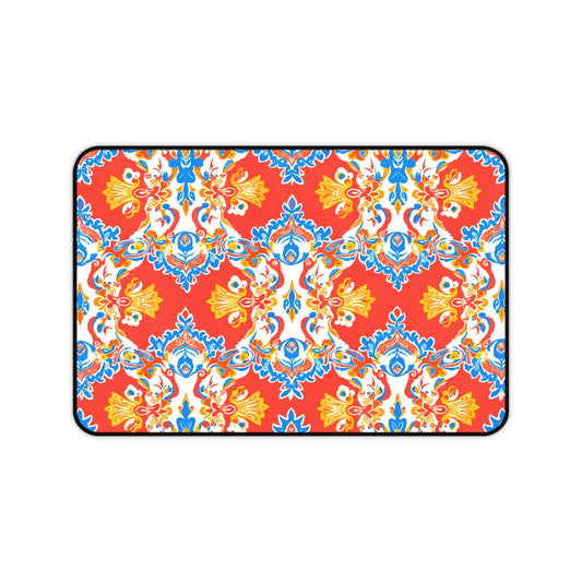 Rectangular neoprene desk mat with a bold red background features an ornate, symmetrical floral and vine pattern in blue, yellow, and white. This vibrant, Mediterranean-inspired non-slip desk pad is a perfect colorful workspace accessory.