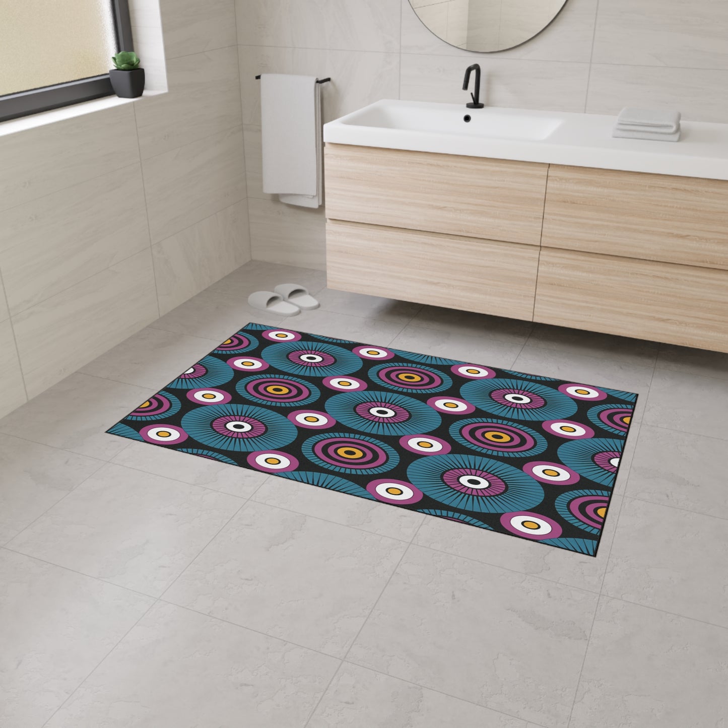 A modern bathroom with light beige tiles, a wooden vanity with a white sink, and a round mirror. The colorful rectangular rug features concentric circles in blue, teal, yellow, red, and white and boasts non-slip rubber backing for safety.