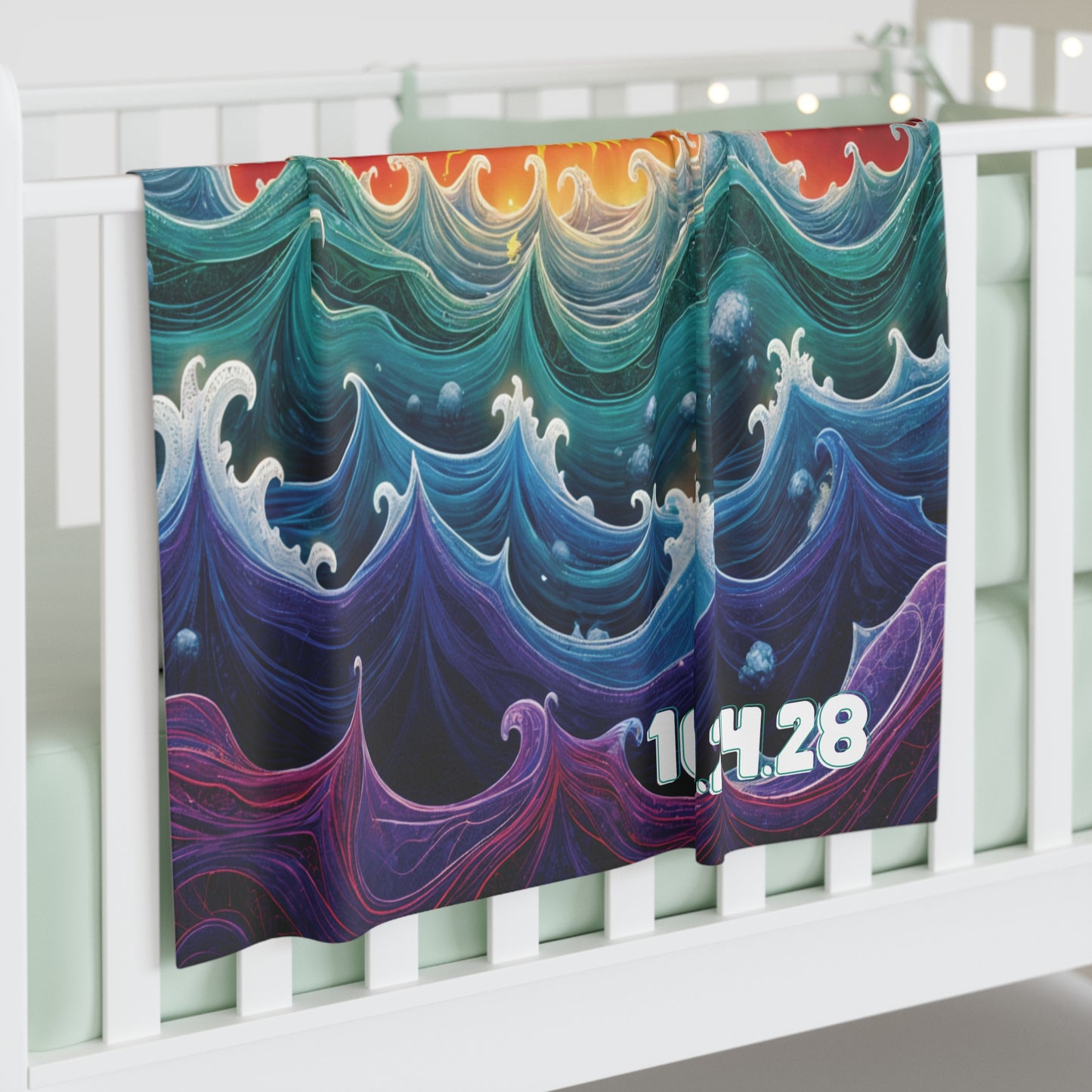 A colorful personalized baby blanket with swirling, stylized ocean waves in blue, green, and purple hues hangs over a white crib rail. The number “10.14.28” appears in bold white text. Soft string lights and pastel bedding are visible in the background.