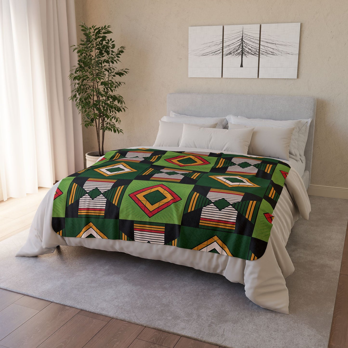A neatly made bed showcases an African-inspired fleece blanket with vibrant geometric patterns in green, black, yellow, red, and white. The cozy home decor features a gray upholstered headboard, white bedding, a potted plant, and minimalist wall art.