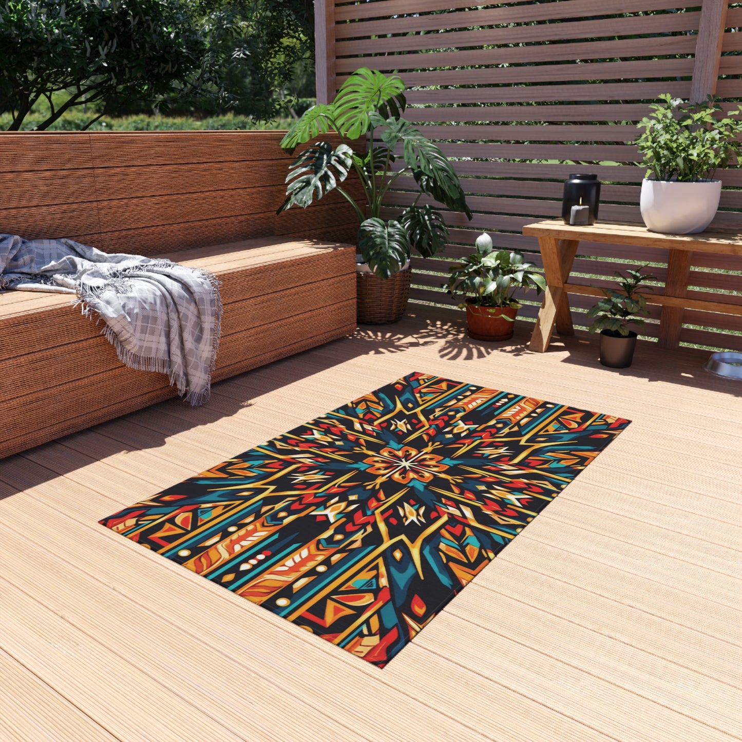 A stylish patio with wooden flooring features an African-inspired outdoor rug in bold reds, blues, and yellows. There’s a wooden bench with a gray throw, several green potted plants, slatted fencing, and sunlight filtering through trees in the background.