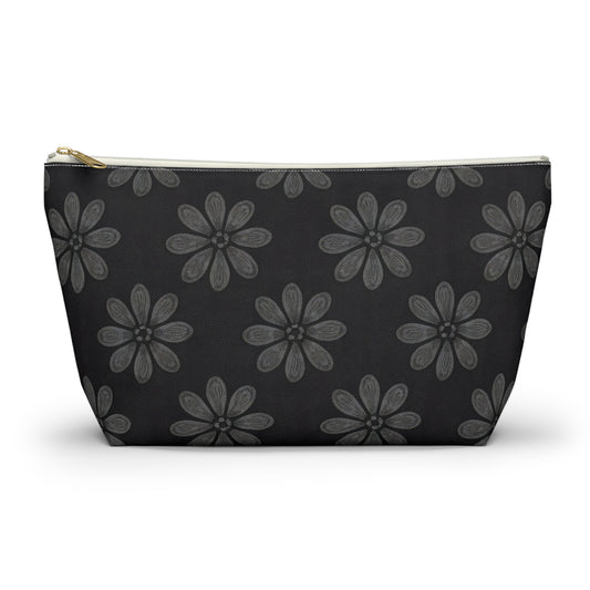 A medium-sized T-bottom pouch featuring a bold, African-inspired pattern of large gray six-petaled flowers on solid black. With a gold zipper and white trim, this chic cosmetic travel bag is displayed elegantly on a white surface.