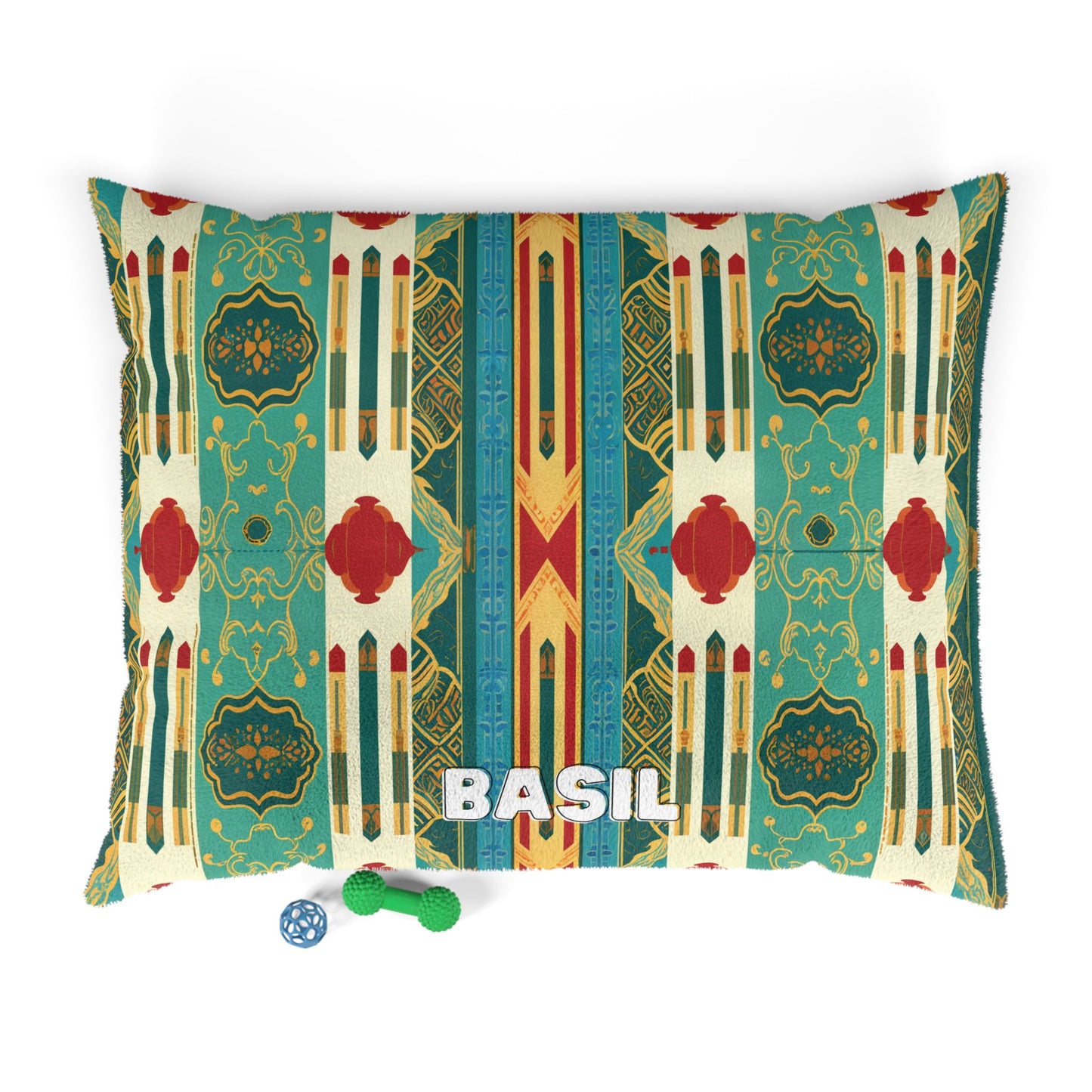 A rectangular dog bed with a geometric teal, red, and gold pattern offers luxurious comfort. BASIL is embroidered in white capital letters at the center. In front of the bed are a blue ball with holes and a green textured bone-shaped dog toy.