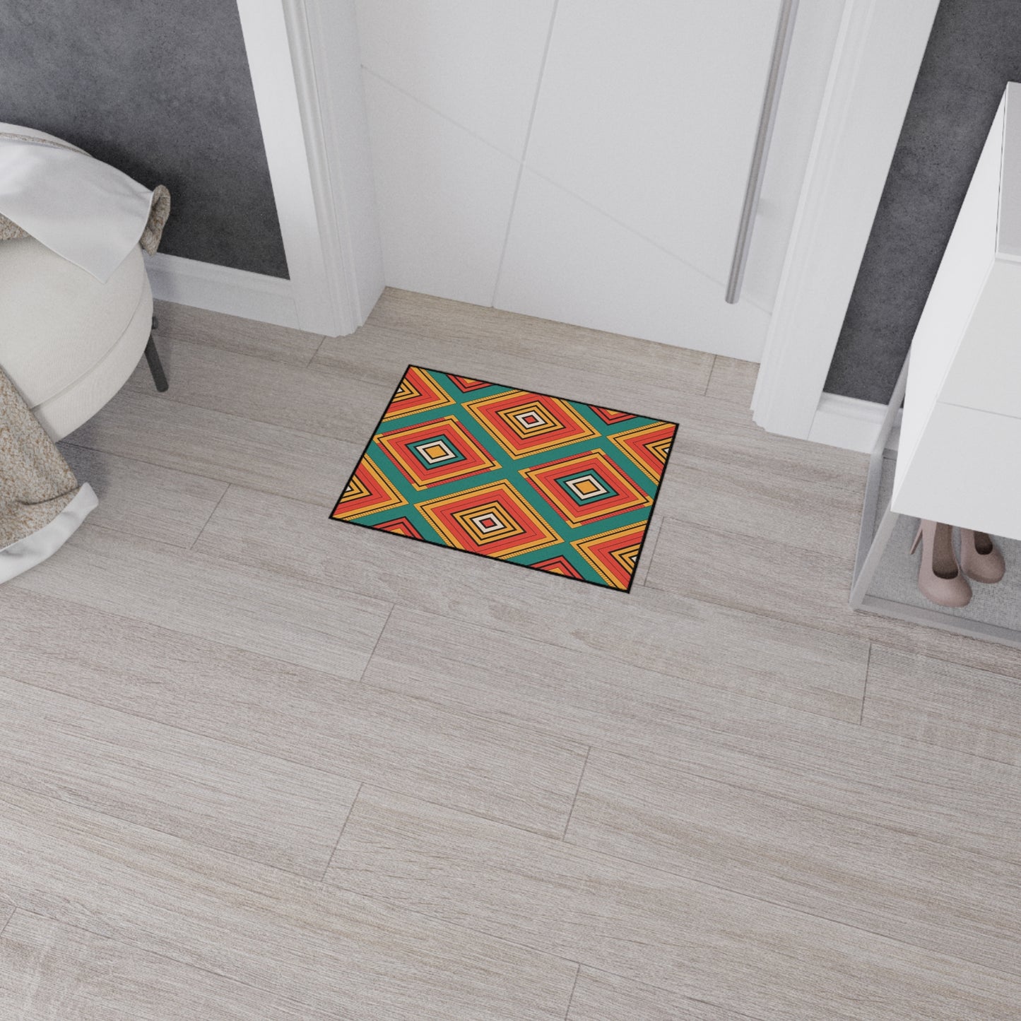 A colorful rectangular rug with an African-inspired geometric diamond pattern in red, orange, yellow, blue, and green lies on a light wood floor near a white door. A white tufted chair and a shoe rack with beige high heels are visible nearby.