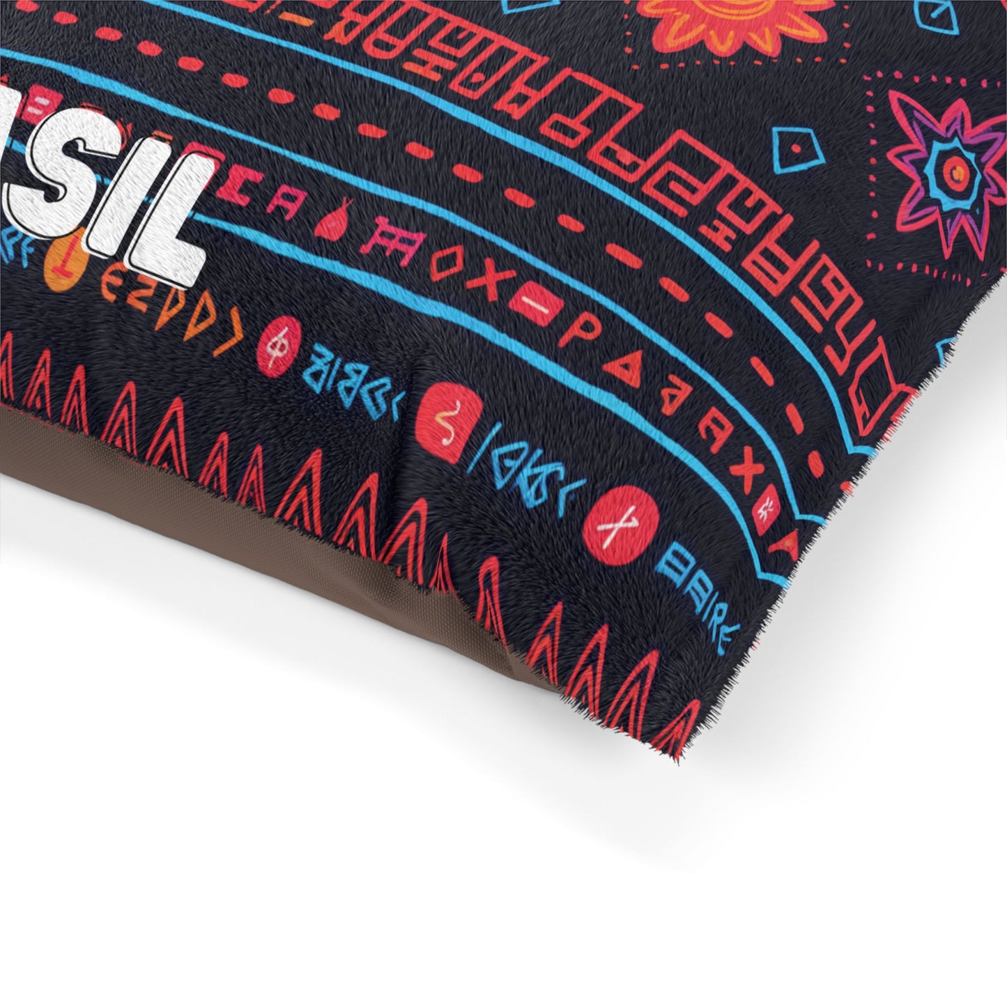 A close-up of a fabric with a colorful, African-inspired geometric and rune-like pattern in red, blue, and orange on a black background. Part of a white embroidered word and several stylized flowers and symbols are visible along the edge.