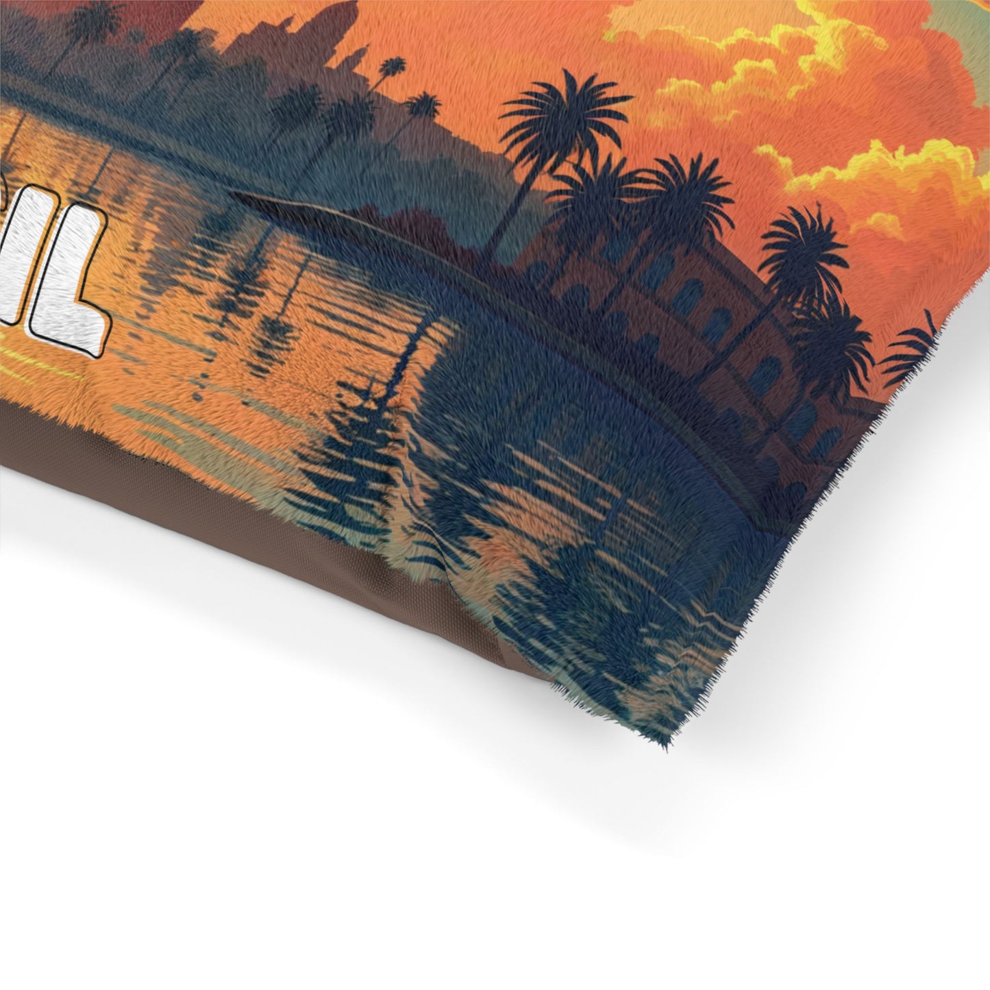 A close-up of a pillow with a printed design of a sunset over a cityscape. Palm trees and buildings are reflected in calm water, while vibrant clouds fill the sky. Enjoy luxurious comfort with durable construction and bold white text on the left side.