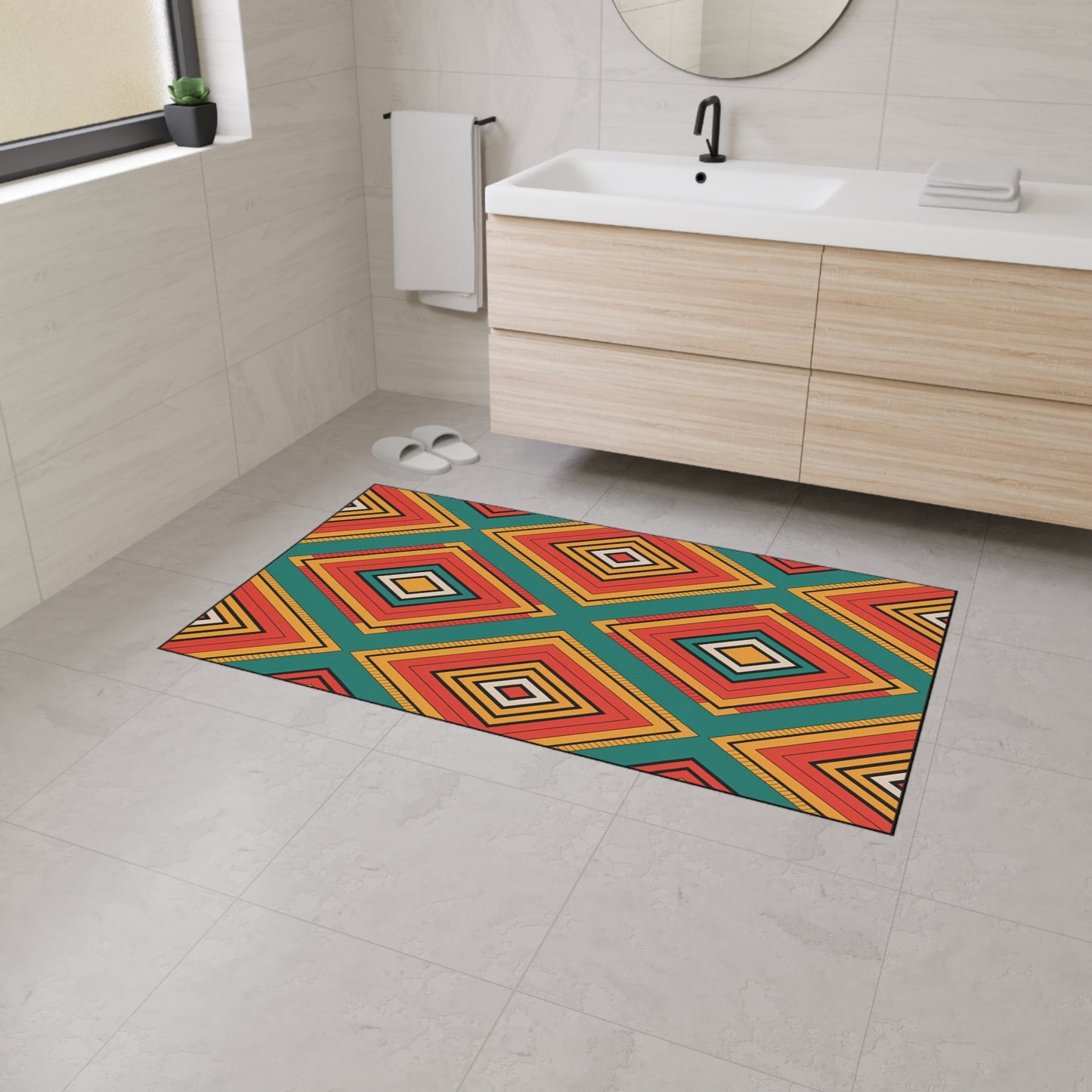 A modern bathroom with light beige tiles, a wooden vanity with a white sink, a round mirror, and an African-inspired geometric bath mat featuring red, yellow, orange, blue, and green diamond patterns on the non-slip rubber backing floor. White slippers are near the vanity.
