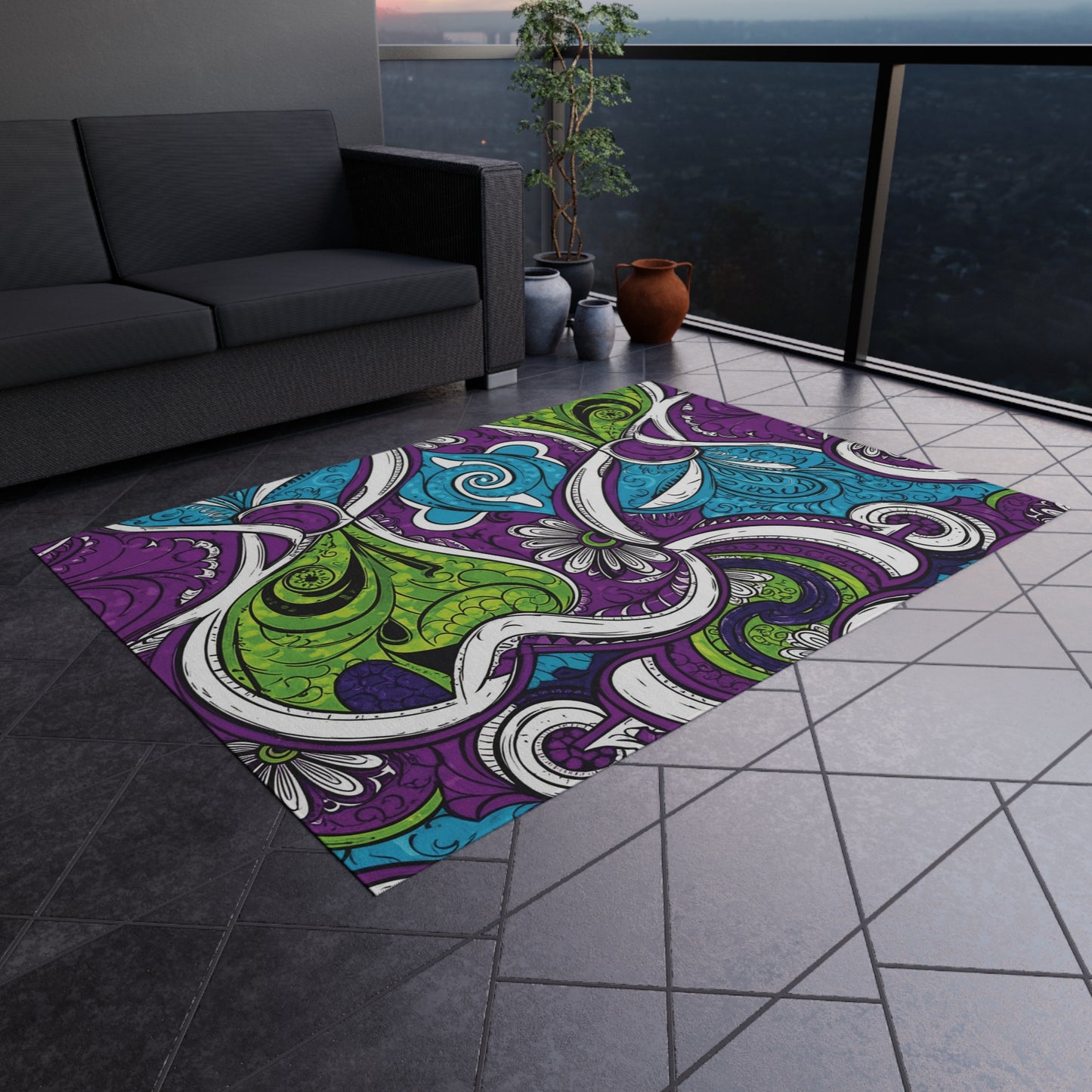 A modern balcony with a dark gray tile floor features a weather-resistant rug in swirling abstract patterns of purple, green, blue, and white. A gray sofa sits on the left, while a potted plant rests near the glass railing overlooking the cityscape.