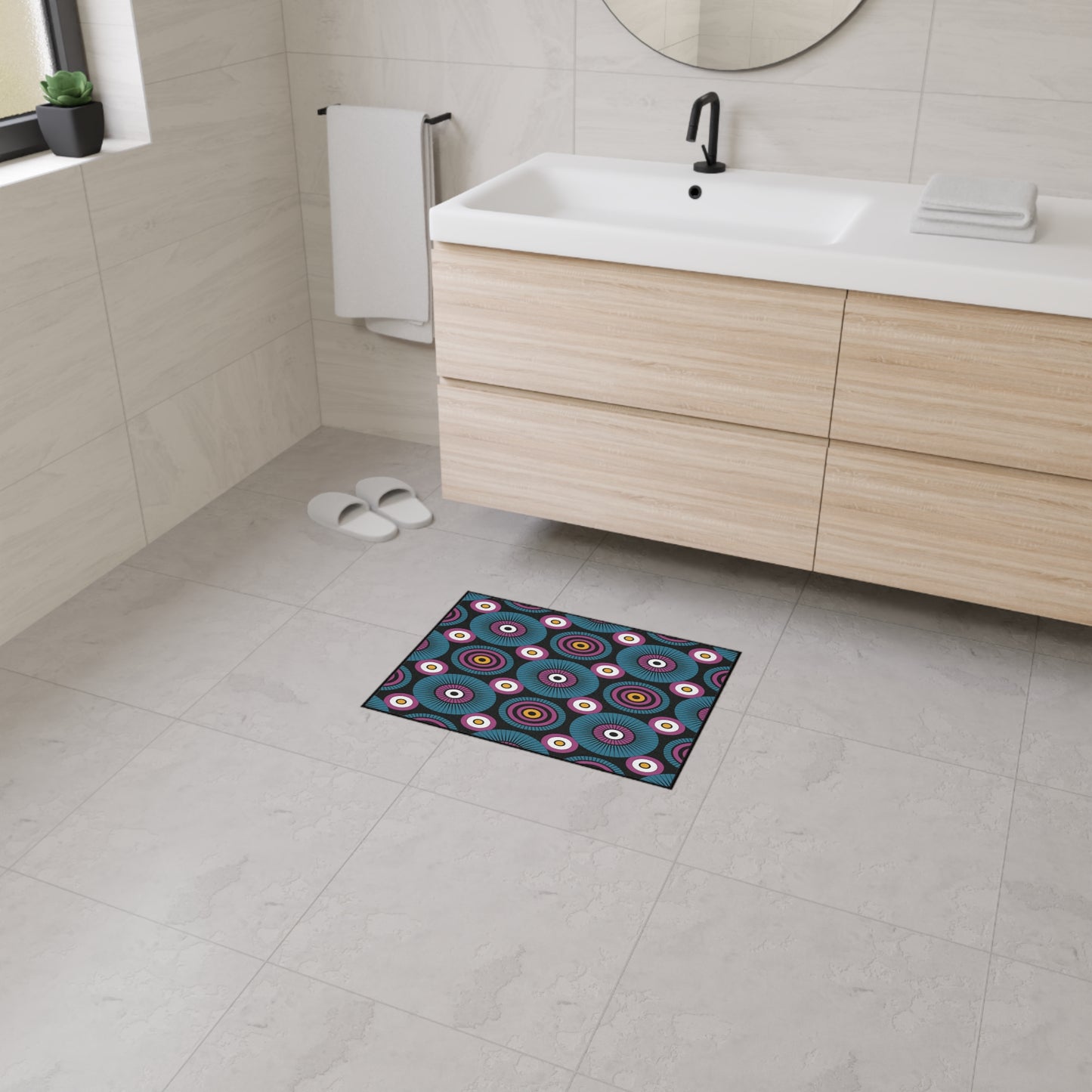 A modern bathroom with light gray tiled walls and floor, a floating wood vanity with a white sink, a round mirror, white slippers, a towel, and a custom floor mat featuring African-inspired aesthetics and non-slip rubber backing for safety.