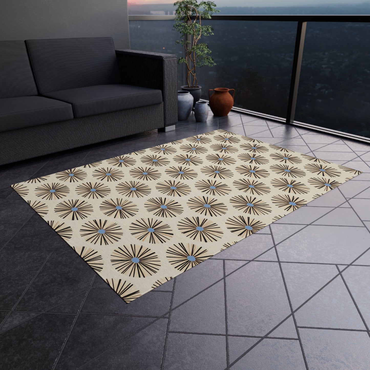 A patterned area rug with authentic African art designs in black, brown, and blue lies on a tiled balcony floor. Nearby are a dark gray sofa, potted plants, and clay pots. A glass railing reveals a hazy, scenic view outside.