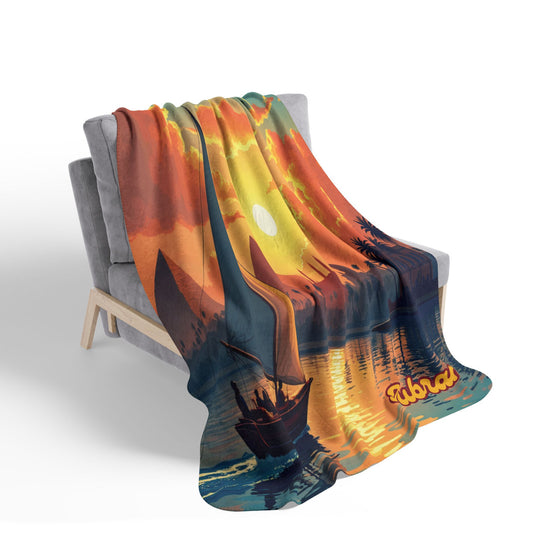 A soft, colorful sherpa fleece blanket with a vivid sunset scene drapes over a modern gray chair. The African-inspired fleece blanket features a boat, palm trees, and orange clouds, with Tubaak printed in orange near the bottom—perfect for home decor.