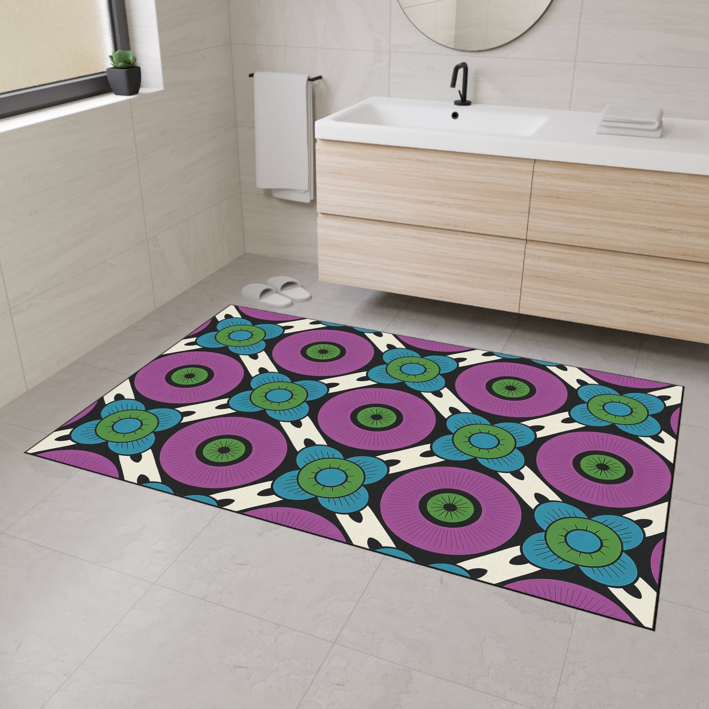 A modern bathroom with light-colored tiled walls and floor, a wooden vanity, and a round mirror features a colorful, African-inspired custom floor mat with a bold geometric pattern in purple, blue, green, and black and non-slip rubber backing.