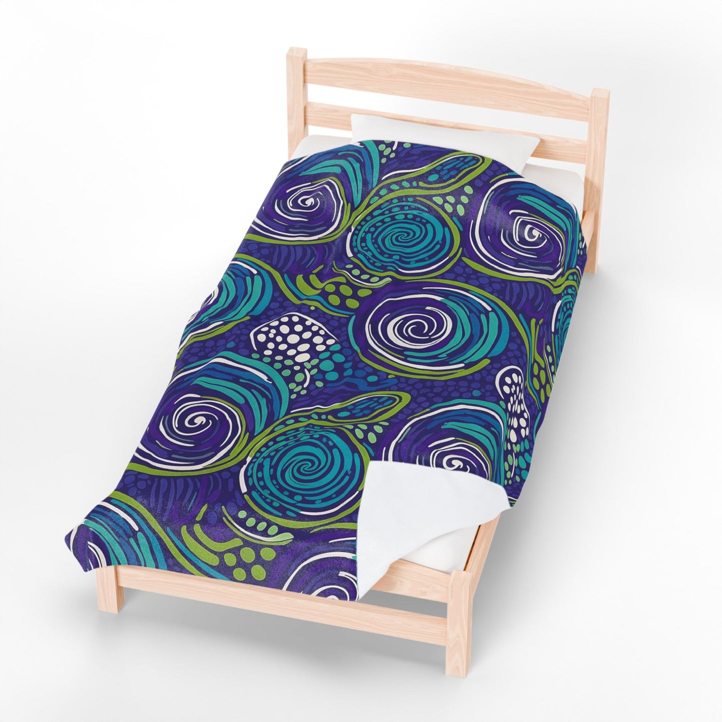 A single wooden bed with a personalized velveteen blanket featuring a bold abstract design of swirling blue, teal, and green patterns with white accents on a dark purple background. The bed has a white pillow and is photographed on a plain white surface.