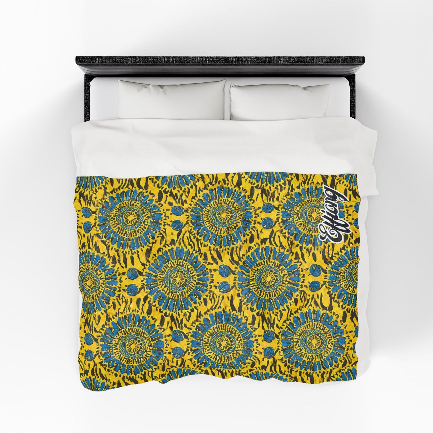 A bed with white pillows and an African-inspired blanket featuring bold yellow, blue, and black abstract circles; “Legacy” is written in stylish white script at the top right corner. The image is viewed from above.