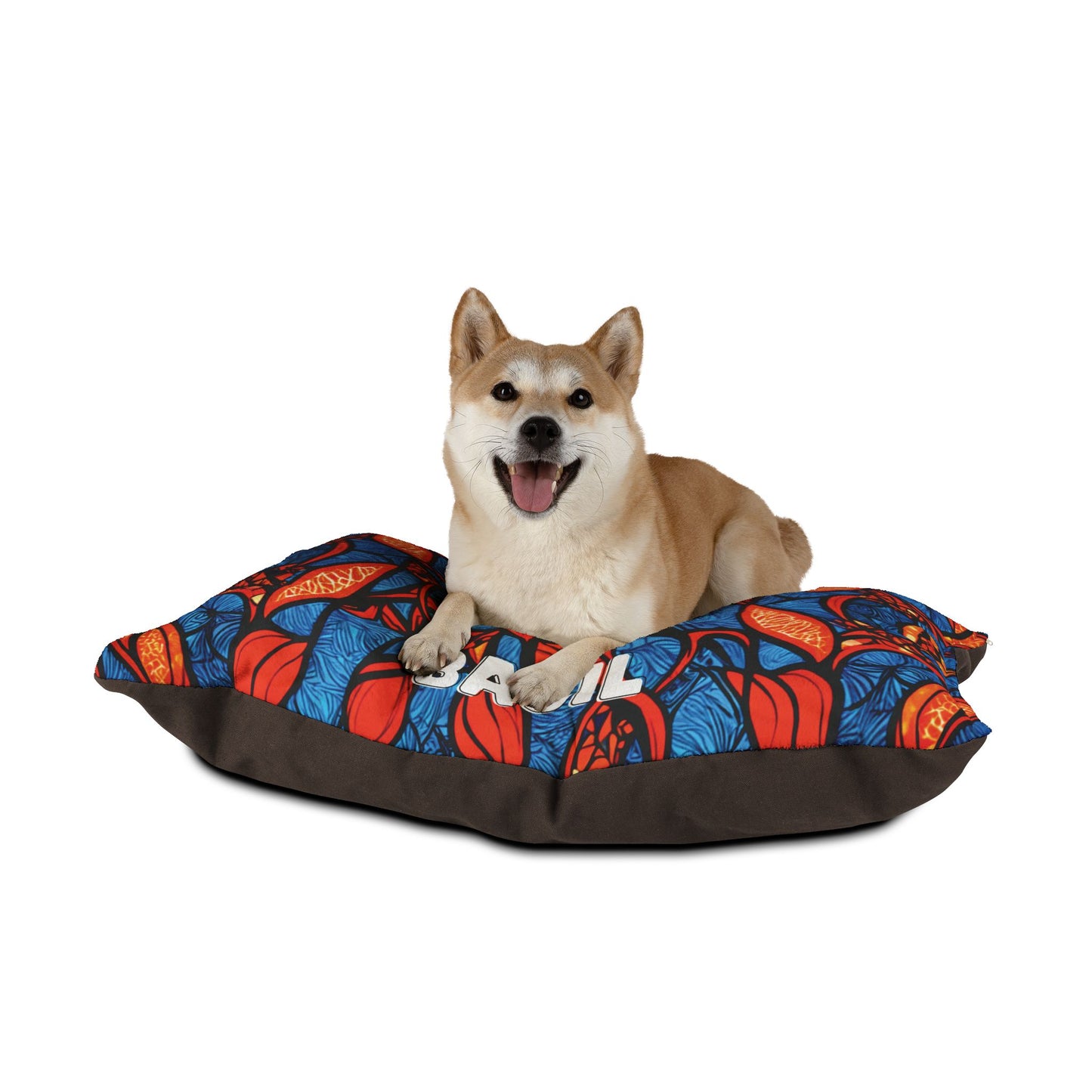 A tan and white Shiba Inu dog lies on a stylish dog bed with red, blue, and orange leaf designs. The happy pup relaxes with its mouth open and tongue out, against a plain white background.