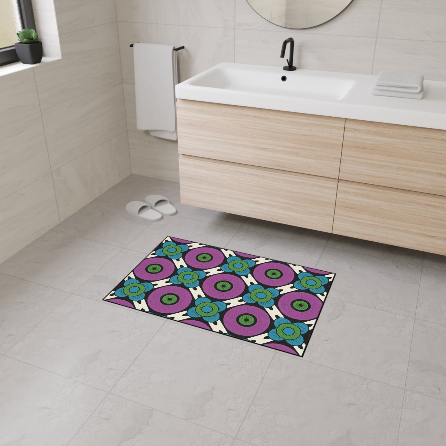 A modern bathroom with beige tile walls and floor, a light wood vanity with a white sink, a round mirror, and a towel rack. The colorful rug features African-inspired aesthetics and non-slip rubber backing. White slippers are by the window.