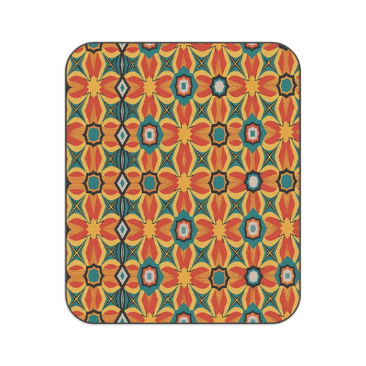 Rectangular object with rounded corners featuring a vibrant, symmetrical pattern. This African-inspired picnic blanket displays red, orange, and yellow flower shapes, teal diamonds, star motifs, and a vertical black line near the left edge.