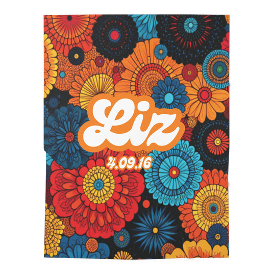A vibrant floral pattern with large, colorful flowers in red, blue, orange, and yellow covers the background of this custom swaddle blanket. In the center, bold white script reads Liz with 4.09.16 below in yellow, all outlined in orange for emphasis.