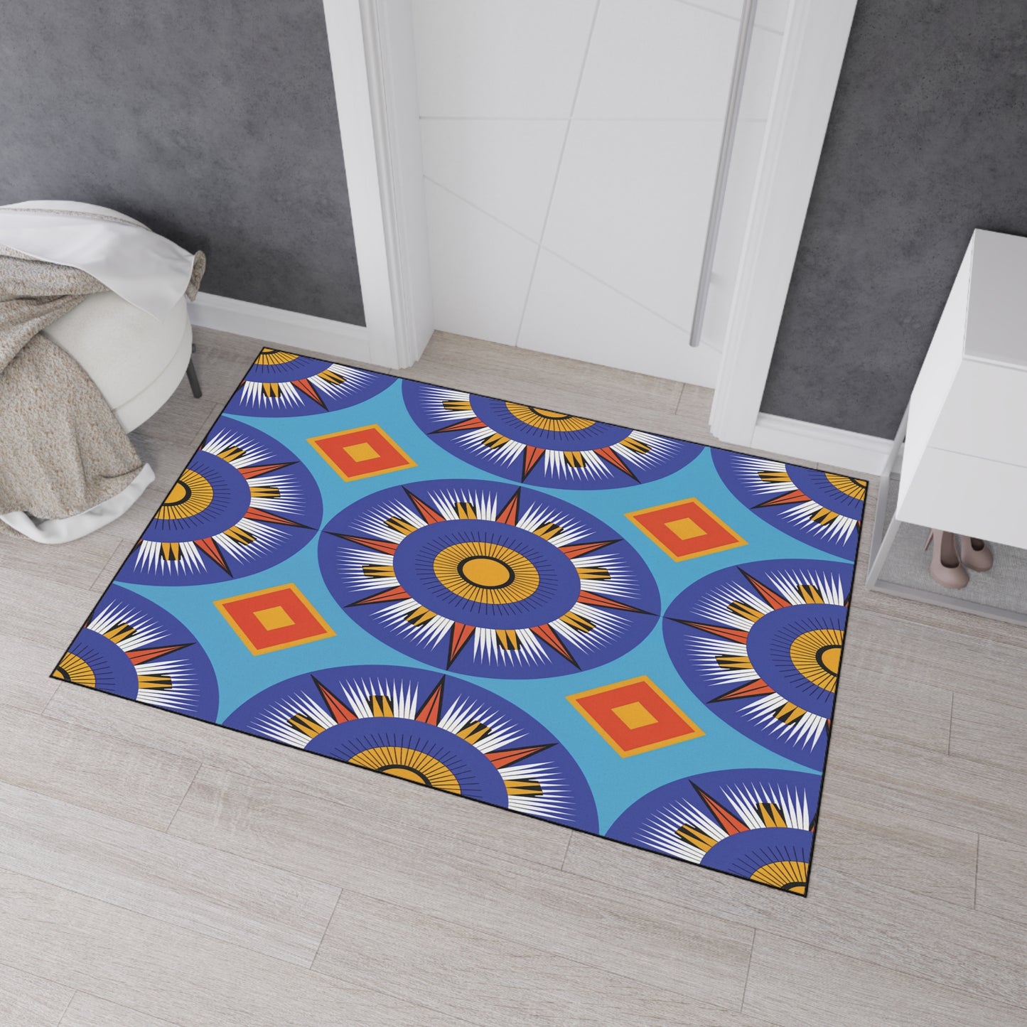 A rectangular rug with vibrant geometric patterns and African-inspired aesthetics lies on a light wood floor. The rug features circular blue, white, yellow, and black starburst designs and red-orange diamonds on a bright blue background.