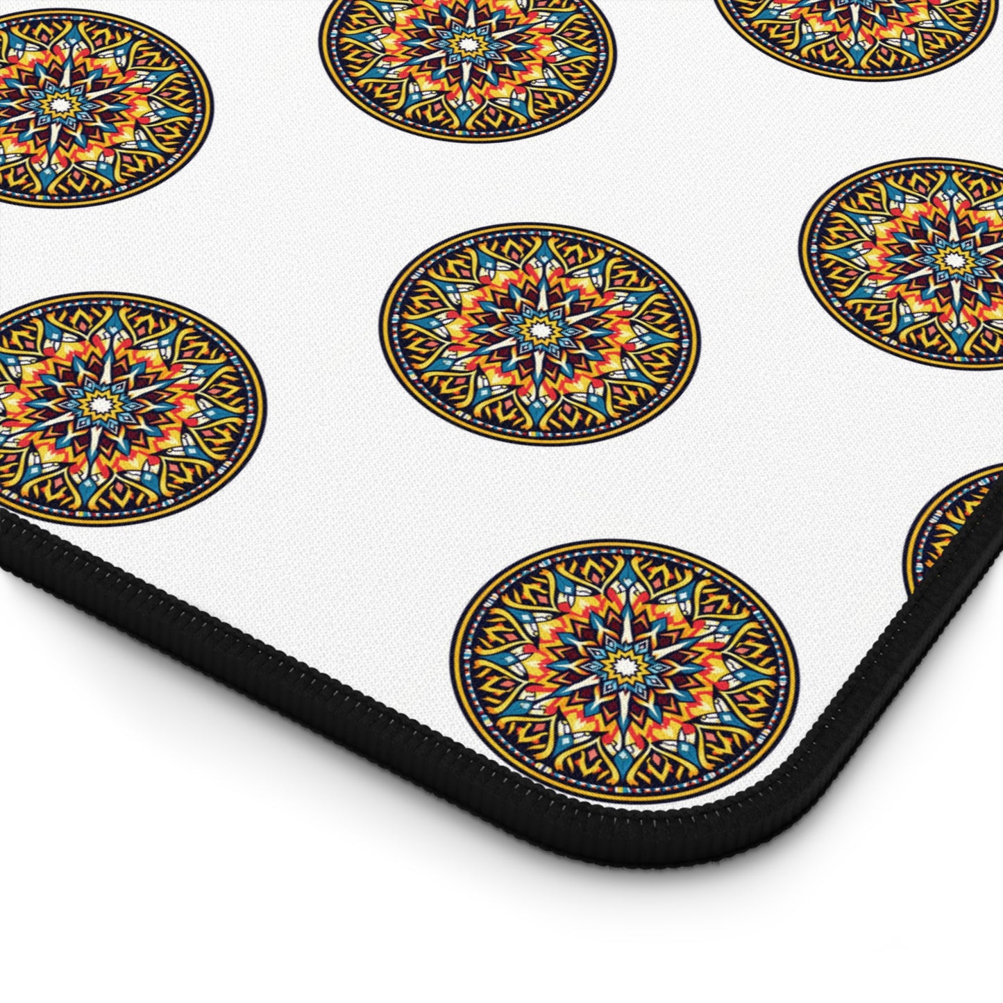A close-up of a neoprene desk mat with a repeating pattern of colorful, circular mandala designs. Each mandala features intricate geometric shapes in blue, orange, red, and yellow, outlined in black. The mat has a black edge.