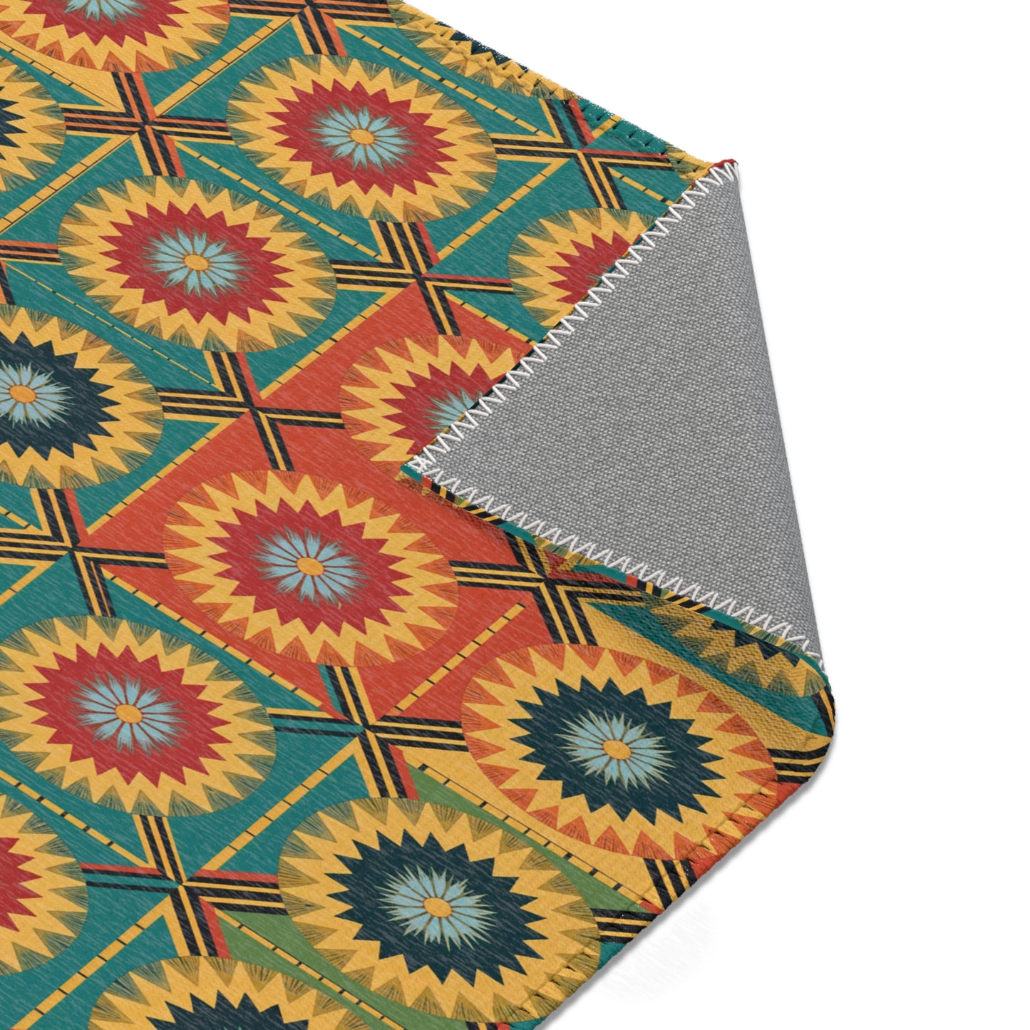 A close-up of a fabric with a vibrant, geometric pattern inspired by African design rugs, featuring circular starburst shapes in yellow, red, orange, and teal. One corner is folded over to reveal durable polyester chenille and zigzag white stitching along the edge.