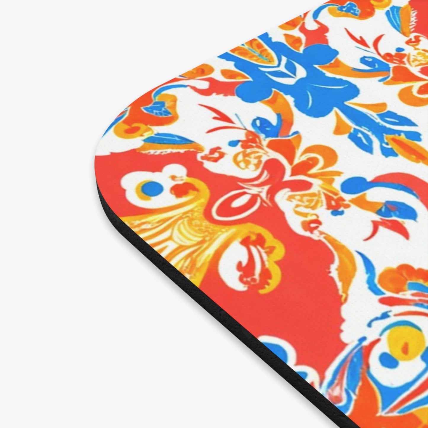 Close-up of an African-inspired mouse pad with a vibrant floral pattern in red, orange, blue, and yellow on a white background. Trimmed in black with a textured fabric surface and non-slip rubber base for secure use.