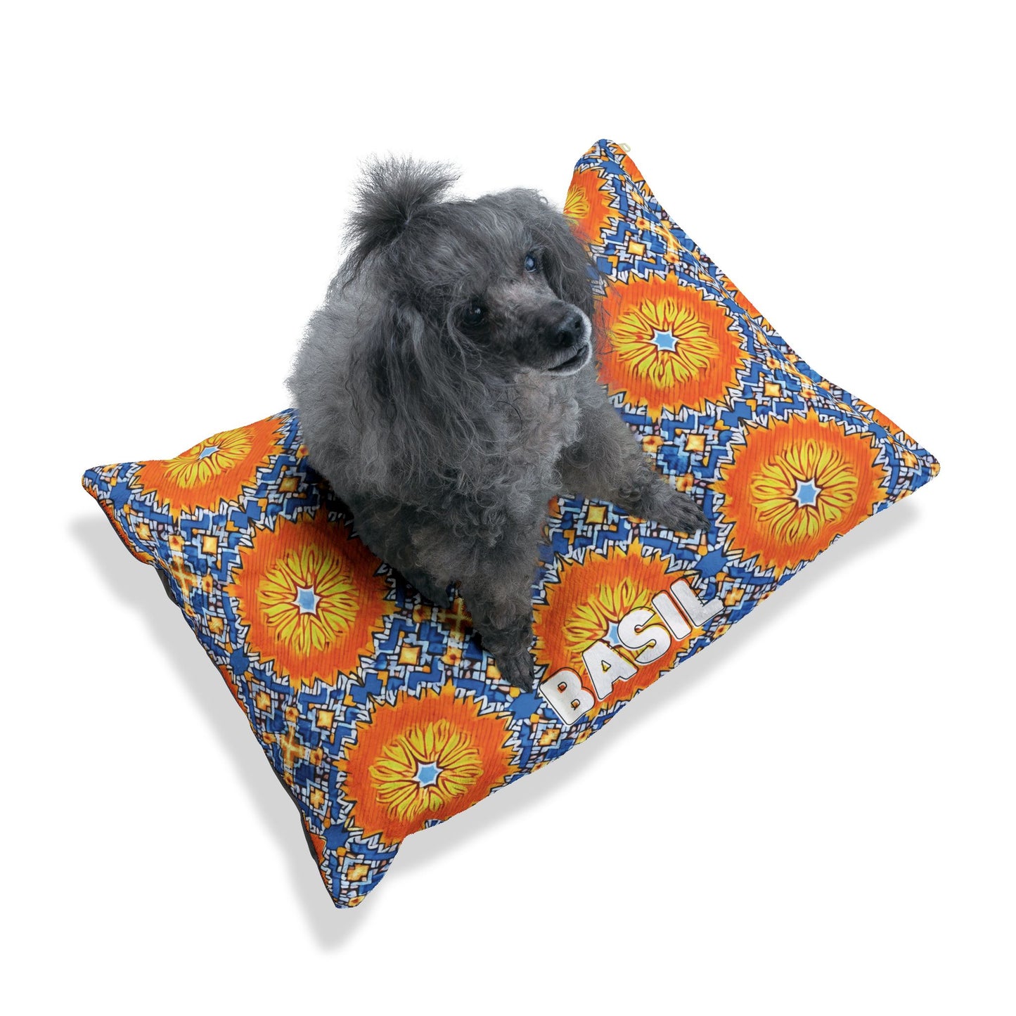 A small gray poodle with fluffy fur sits on a vibrant African inspired pet bed. Featuring orange and yellow sunbursts, blue accents, and BASIL in bold white letters, this personalized pet bed stands out against the crisp white background.