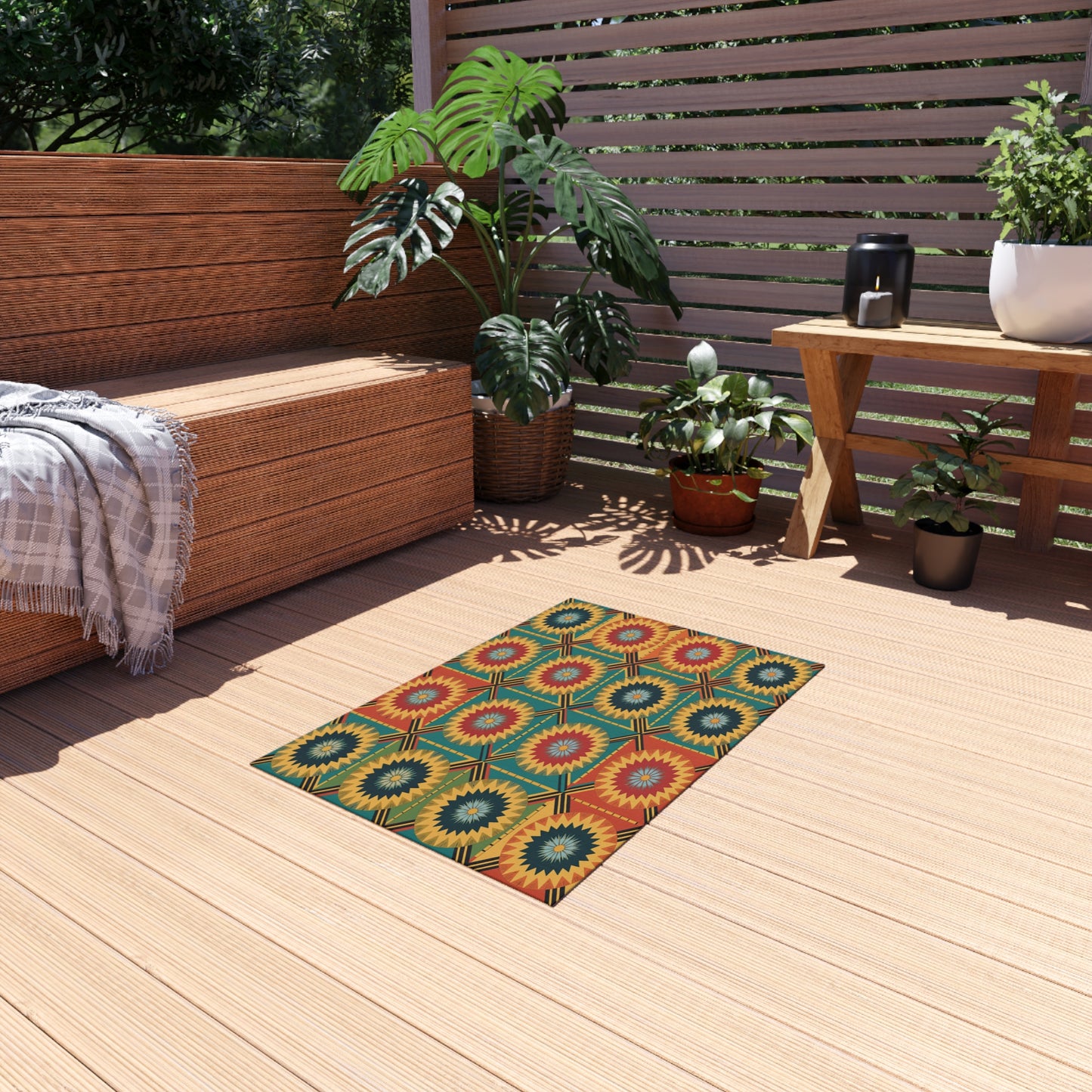 A cozy wooden deck features a woven bench, gray plaid throw, several green potted plants, and a small table with a teapot. An African-inspired outdoor rug with no-skid polyester backing in vibrant tones lies at the center as sunlight filters through wooden slats.