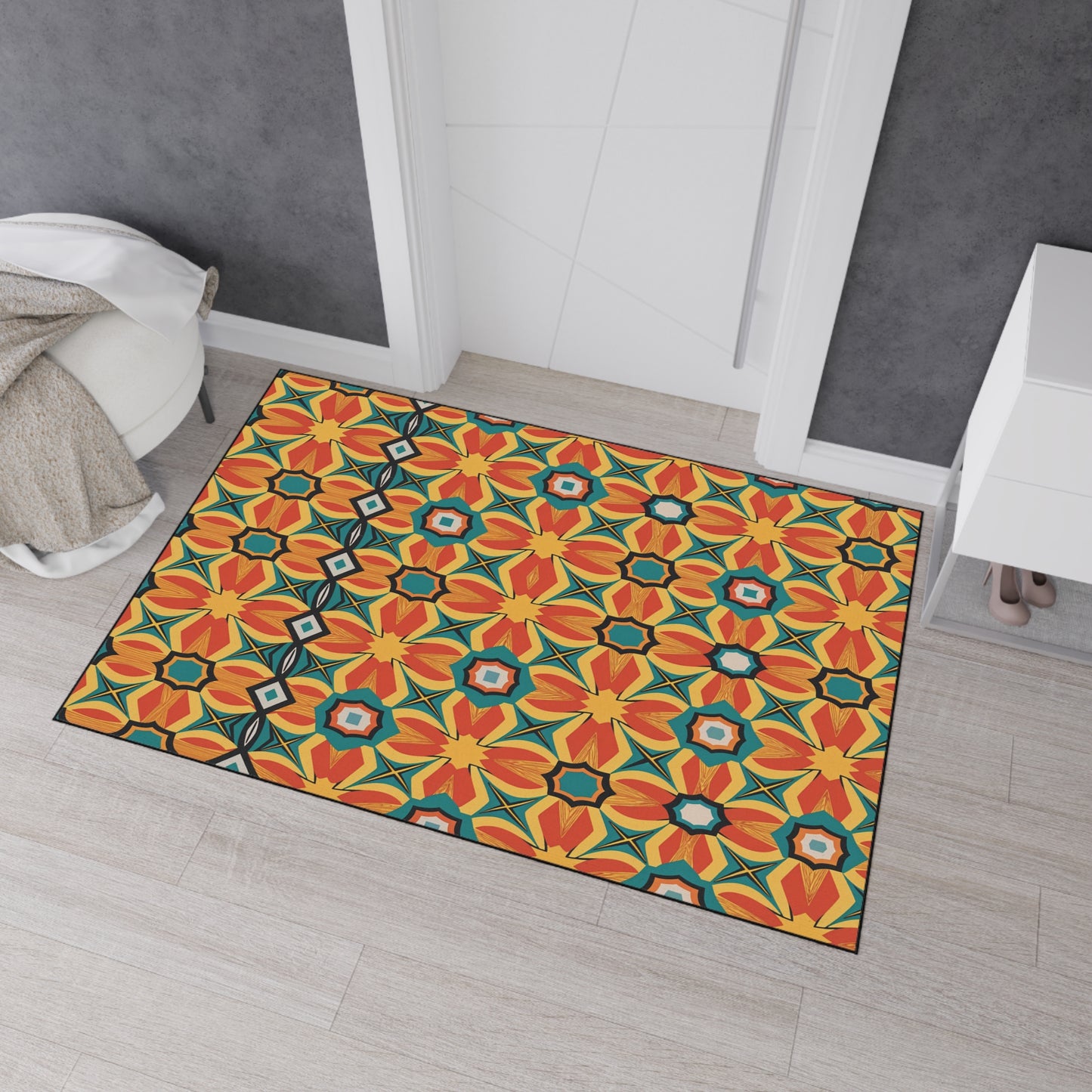 A colorful rectangular rug with bold geometric patterns in red, yellow, orange, blue, and black brings African-inspired aesthetics to a light wood floor near a white door. Its non-slip rubber backing keeps it secure beside the cabinet filled with shoes.