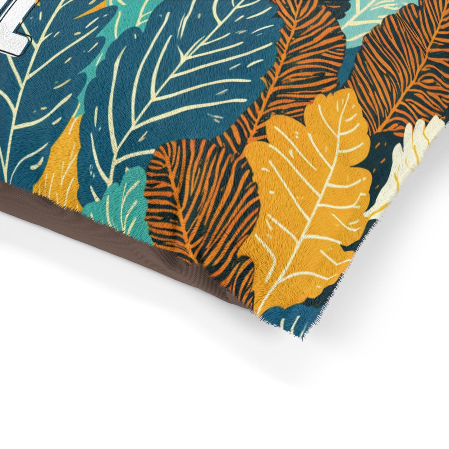 Close-up of a fabric pillow corner with a colorful leaf pattern, showcasing luxurious comfort. Leaves in teal, yellow, orange, and dark blue overlap on a textured surface. The pillow’s brown edge is visible at the bottom left.