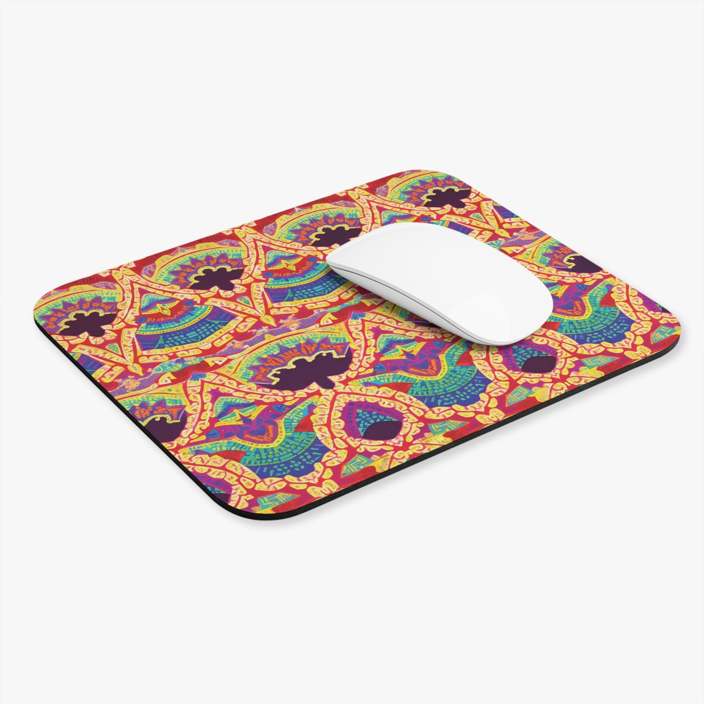 A rectangular African-inspired mouse pad showcases a colorful, symmetrical, abstract pattern in red, yellow, blue, and green on a white background. A white wireless mouse rests near the upper right corner of this vibrant desk accessory.