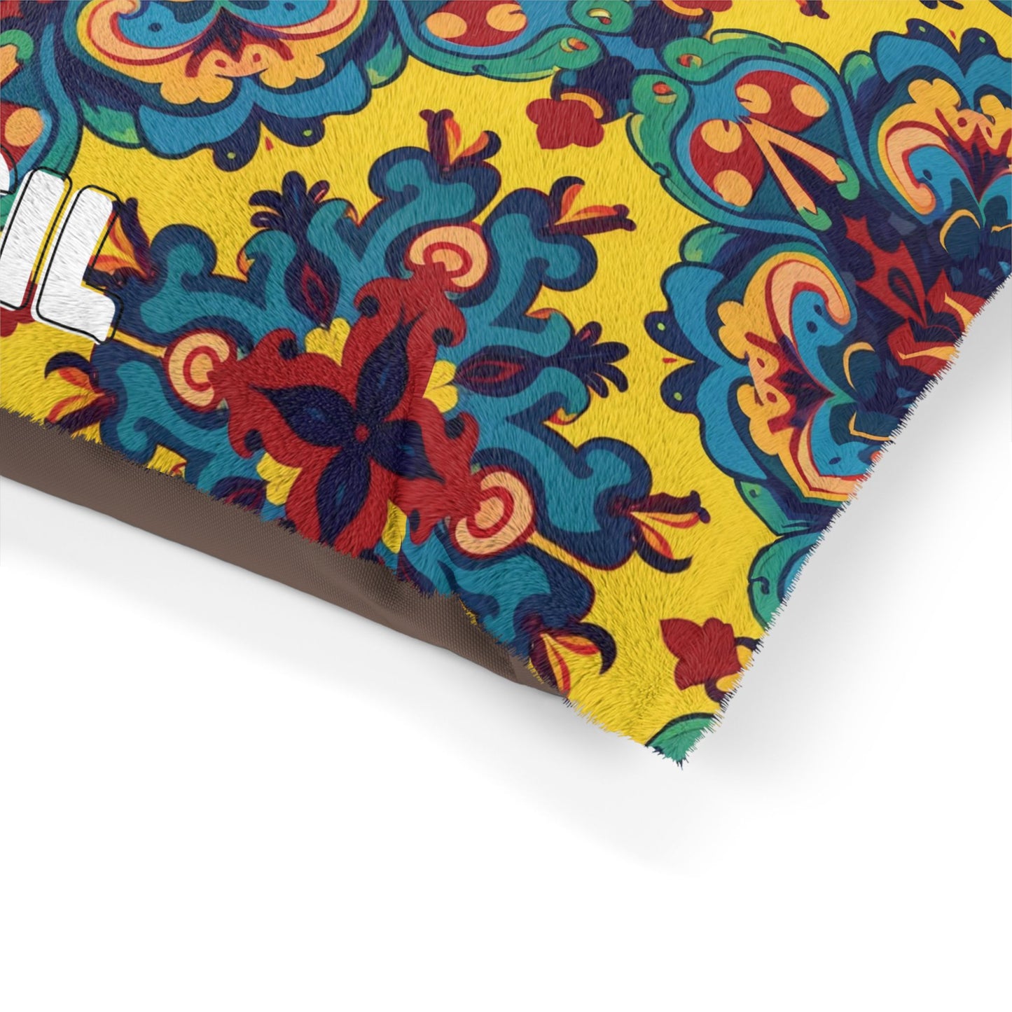 A close-up of a custom pet pillow corner with a vibrant, intricate floral pattern in red, blue, green, and orange on a bright yellow background. Part of a bold white letter “I” is visible, and the edges show a subtle faux-fur texture.