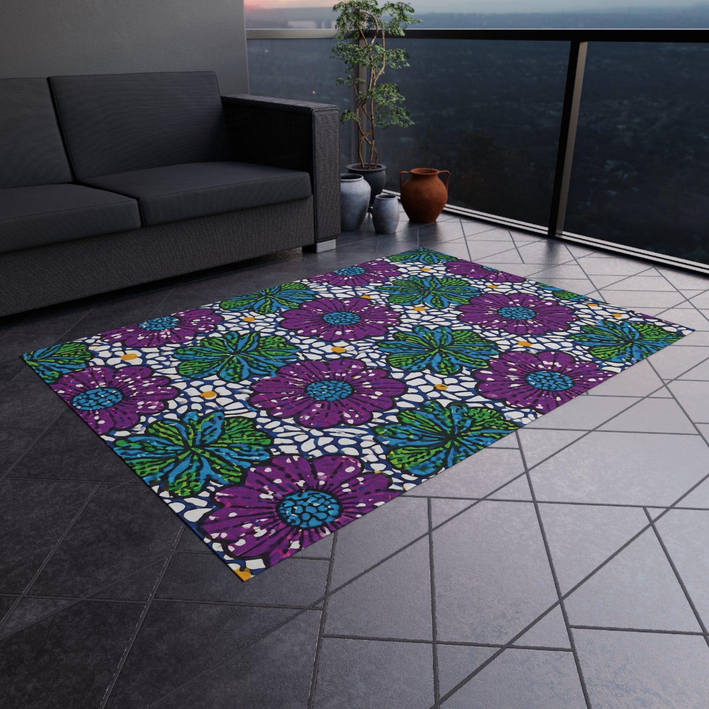A colorful polyester chenille rug with bold purple flowers, blue centers, and green leaves on white brightens a tiled balcony floor beside a dark gray sofa, potted plants, and brown vases, with a cityscape visible beyond the glass railing.