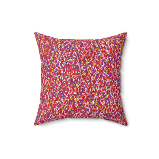 A square African accent pillow with a vibrant, multicolored pattern. Small dots and dashes in red, yellow, purple, and white adorn a red background. The faux suede pillow is set against a plain white surface, viewed from above.