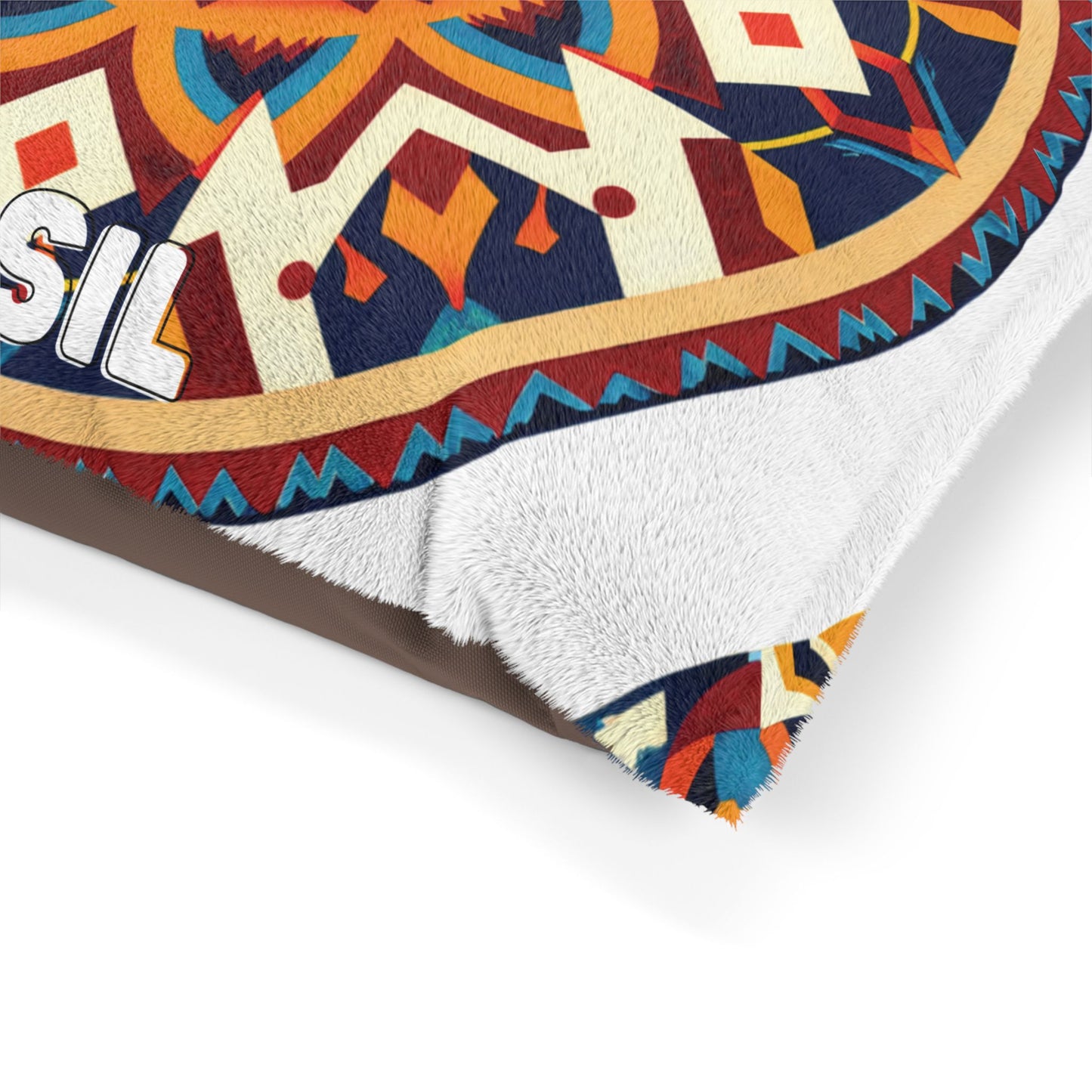 Close-up of a personalized pet bed corner with a vibrant, geometric mandala pattern in orange, blue, red, and cream on top, plus a white, soft, fuzzy underside for luxurious comfort. Partial white text reads SIL. The bed sits on a brown surface.